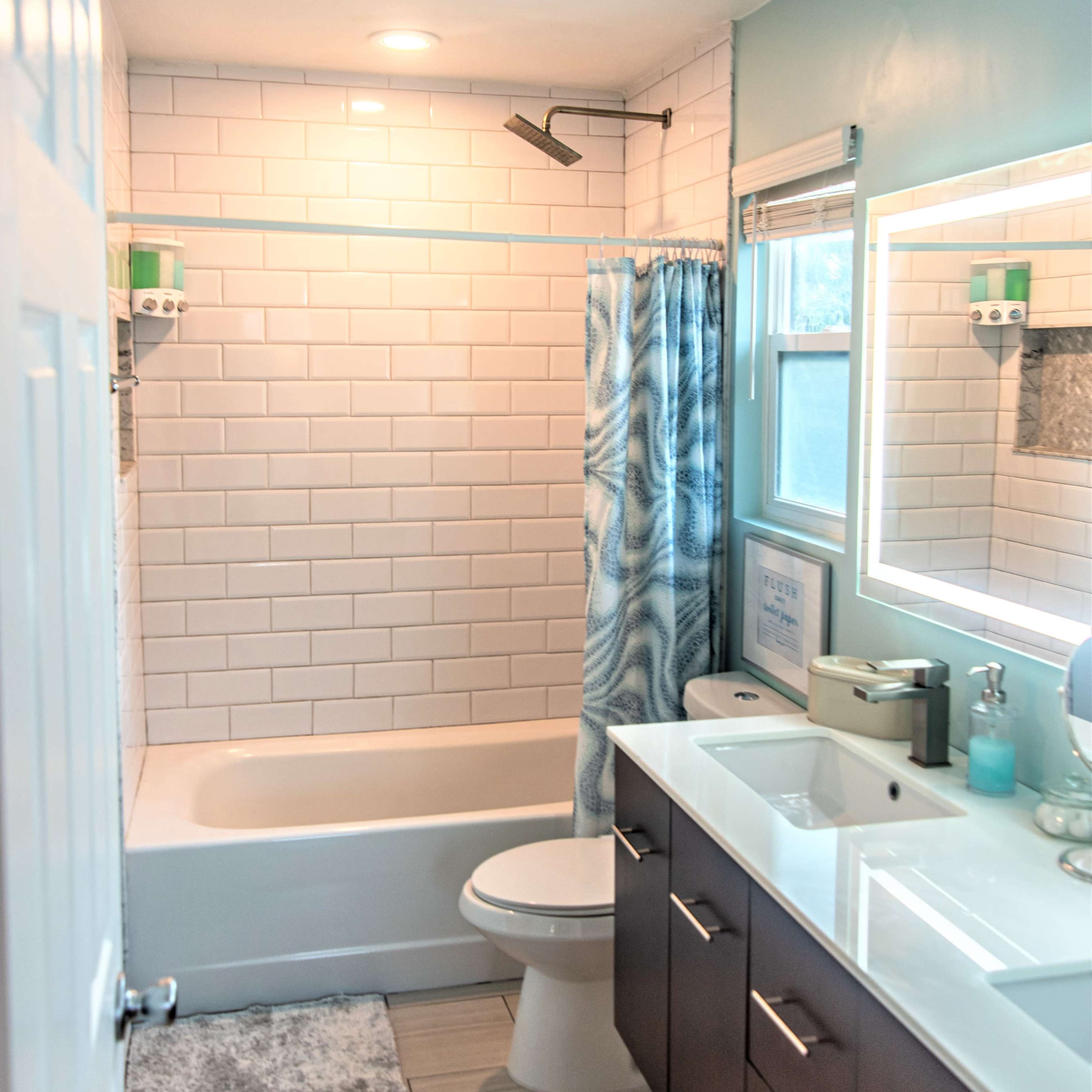 A modern bathroom with a bathtub, shower curtain, toilet, and a double sink vanity with storage underneath.