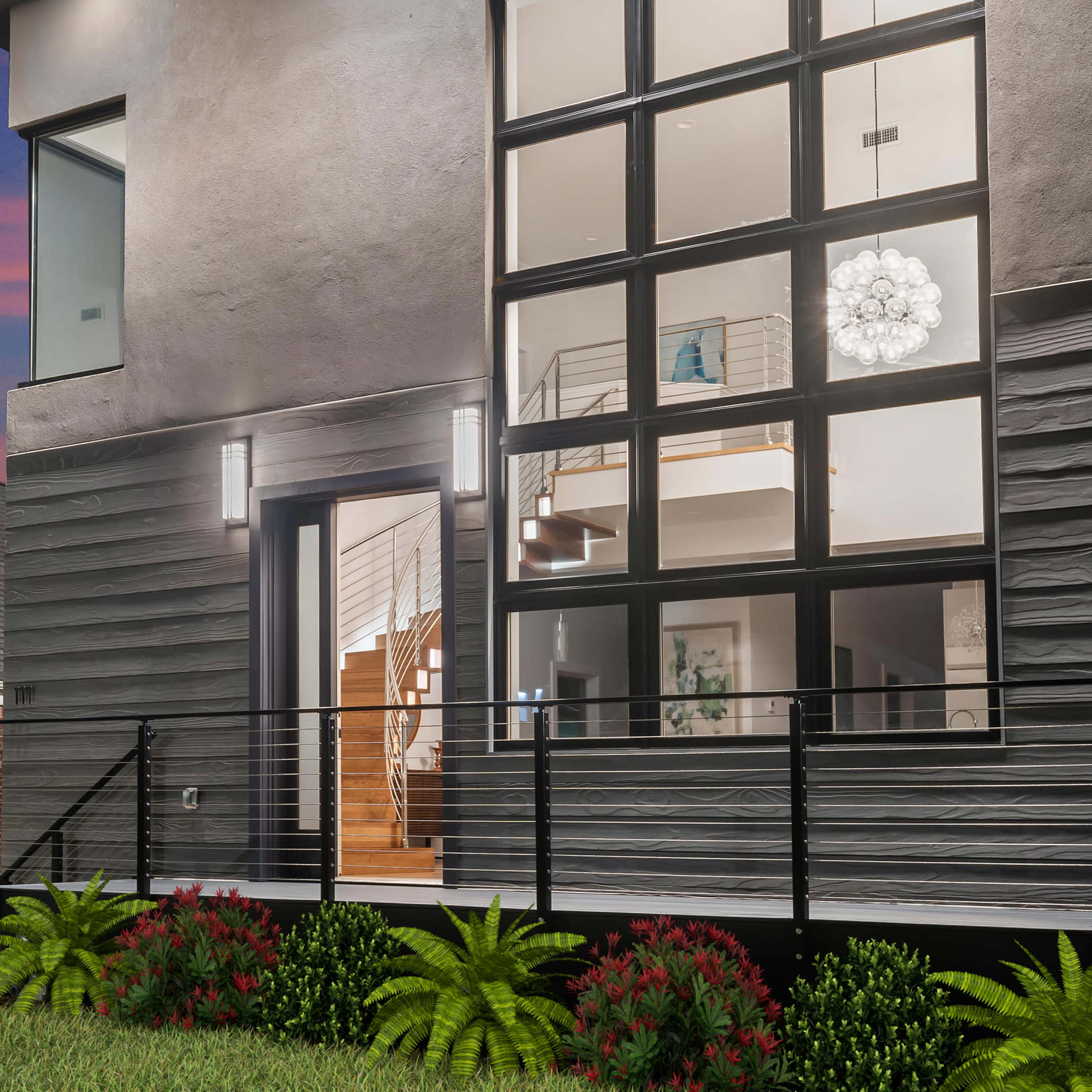 A modern two-story house features large windows and a landscaped yard with shrubs and plants.