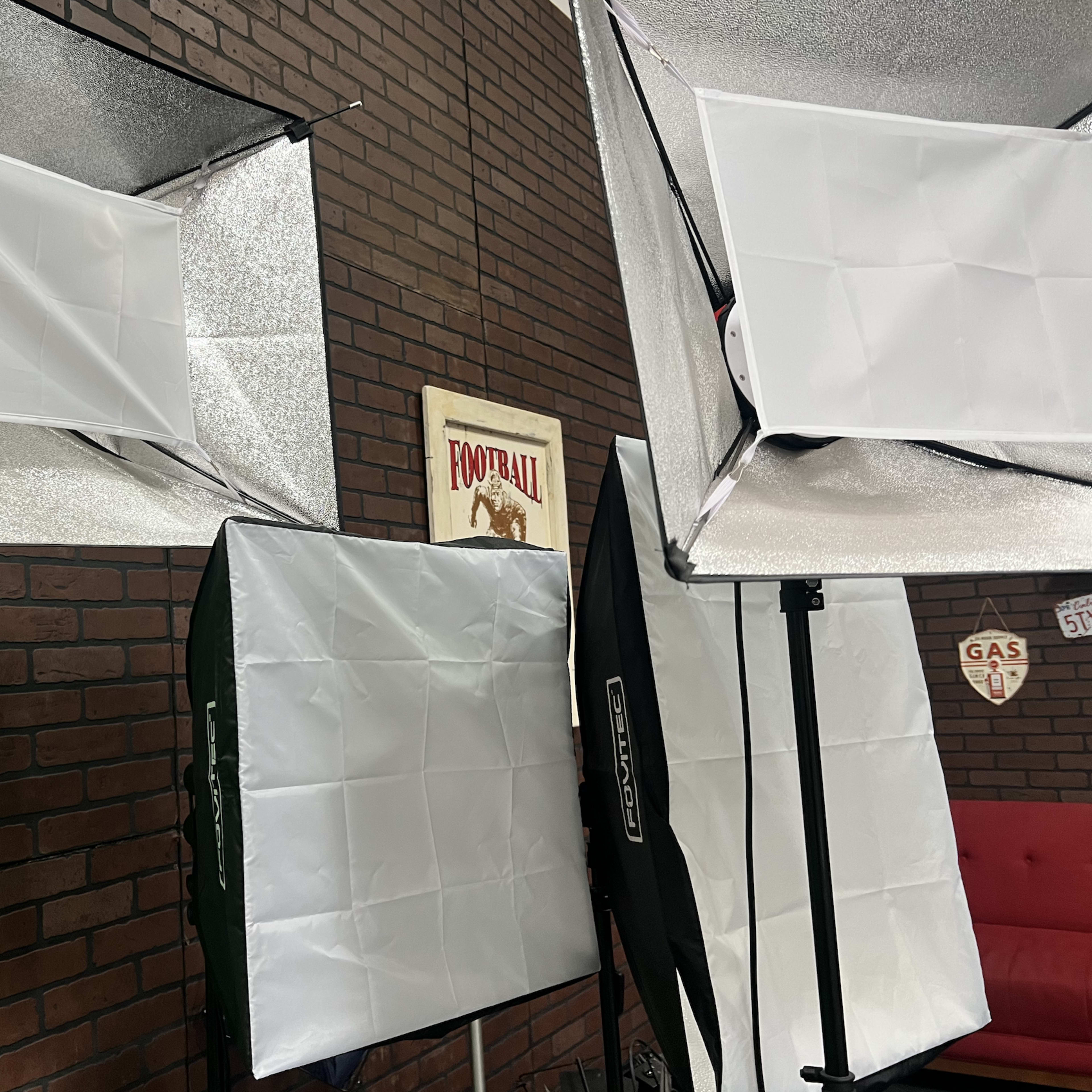 Multiple softbox lighting setups arranged in front of a green screen and a brick wall backdrop.