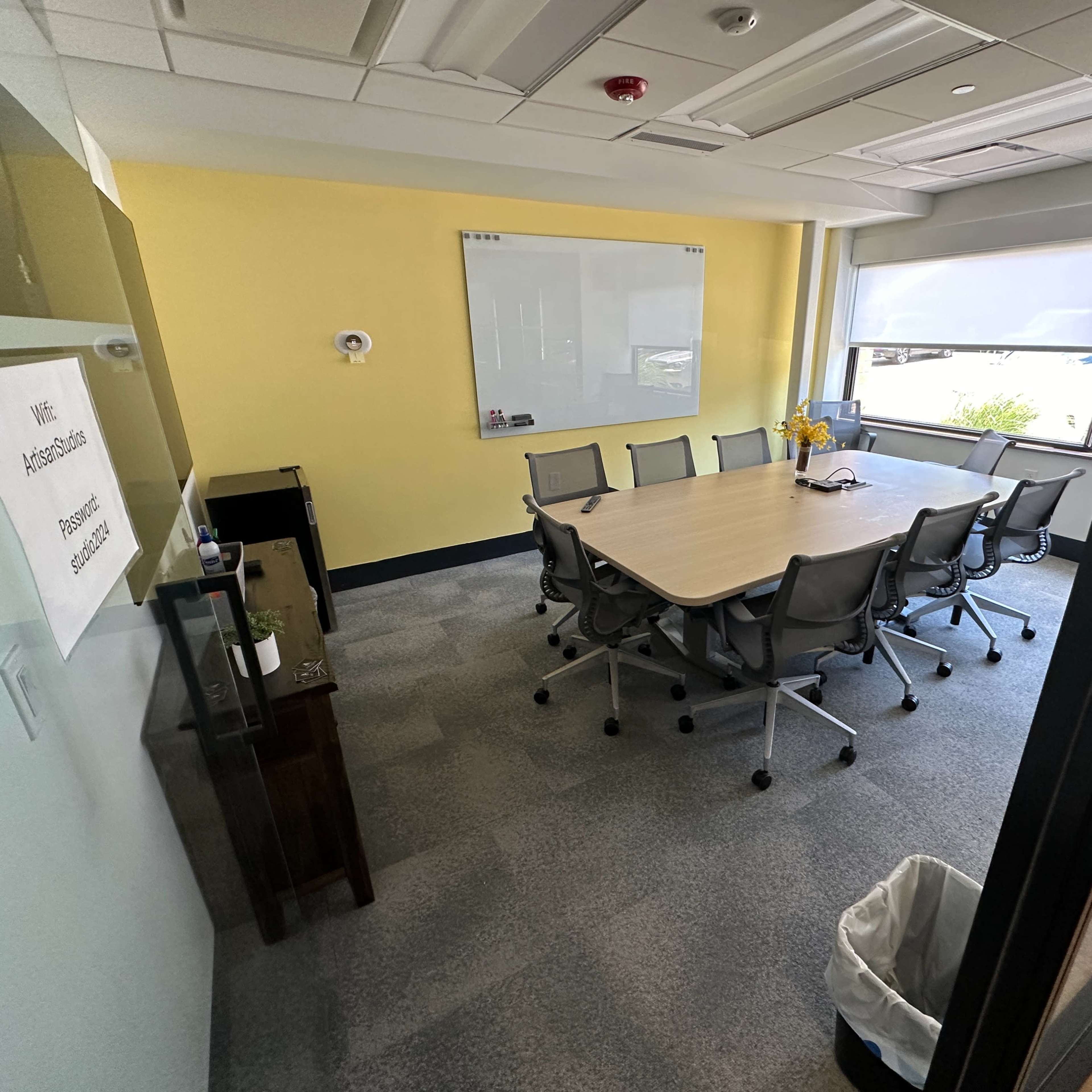 A conference room with a large table surrounded by chairs, a whiteboard on the wall, and a window providing natural light.