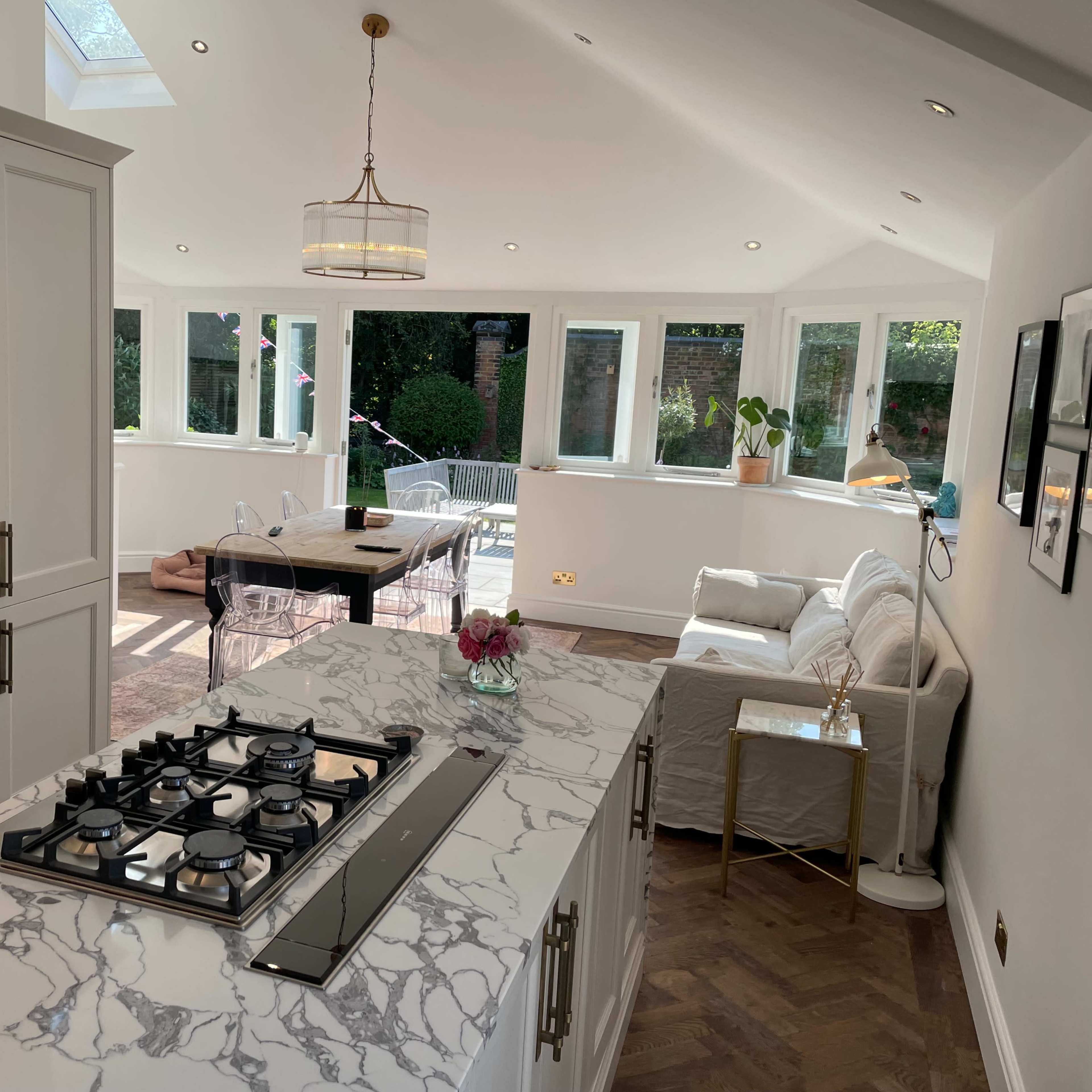 A modern kitchen and living space with a marble countertop, gas stove, and large windows allowing natural light to fill the room.