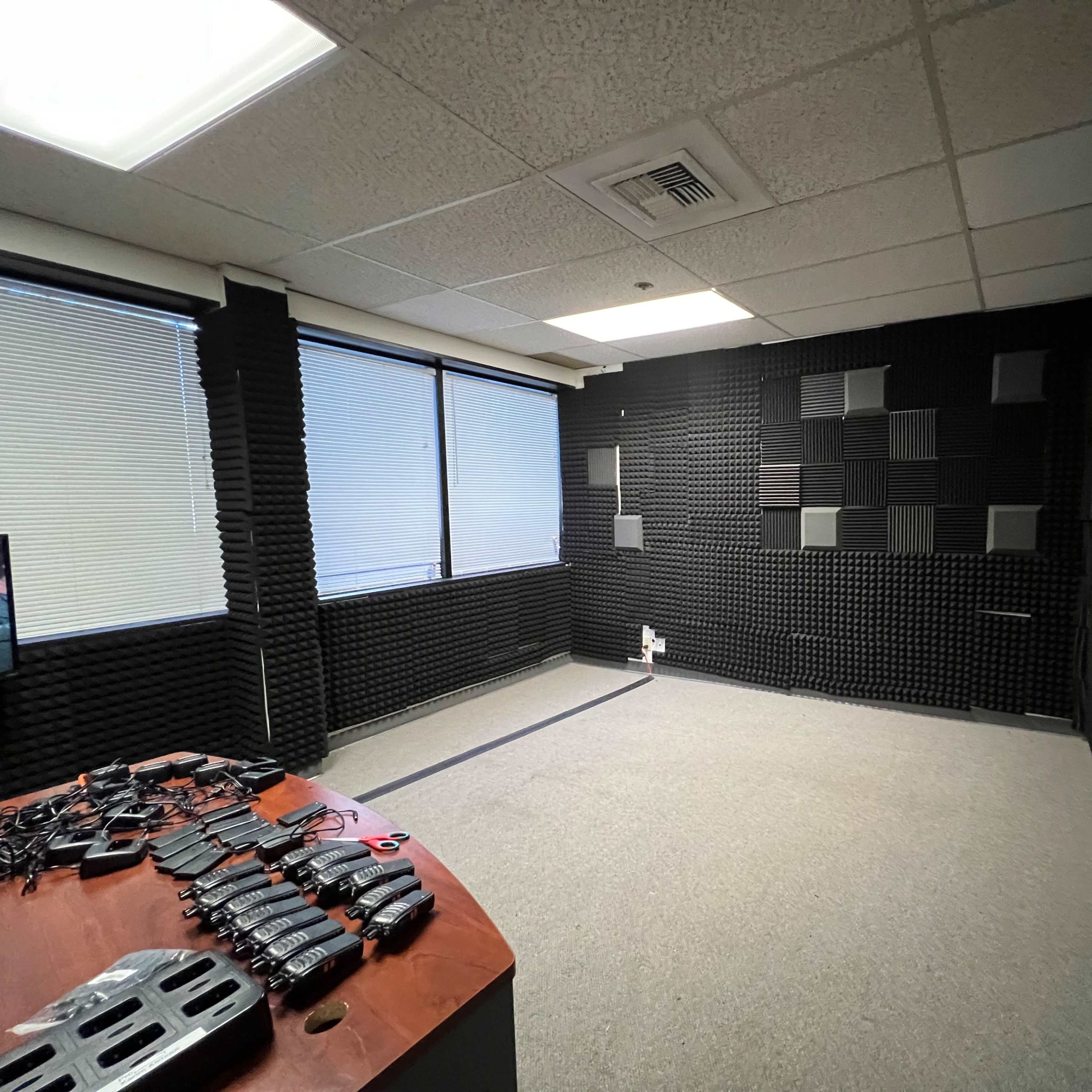 A soundproof room with black acoustic foam panels on the walls, a gray carpet, and a table displaying various tools or equipment.