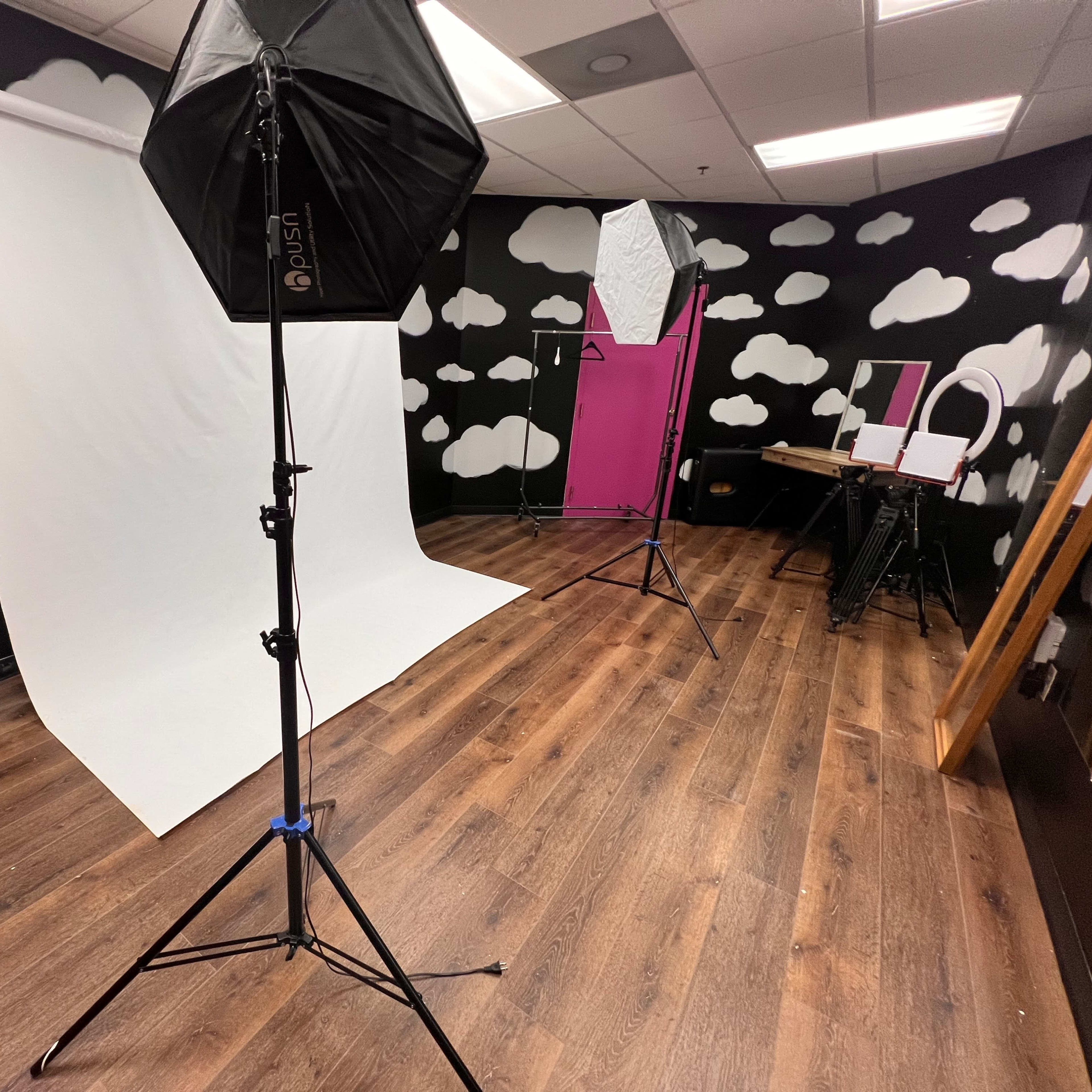 A photography studio featuring a white backdrop, softbox lights, and a black and white cloud-patterned wall.