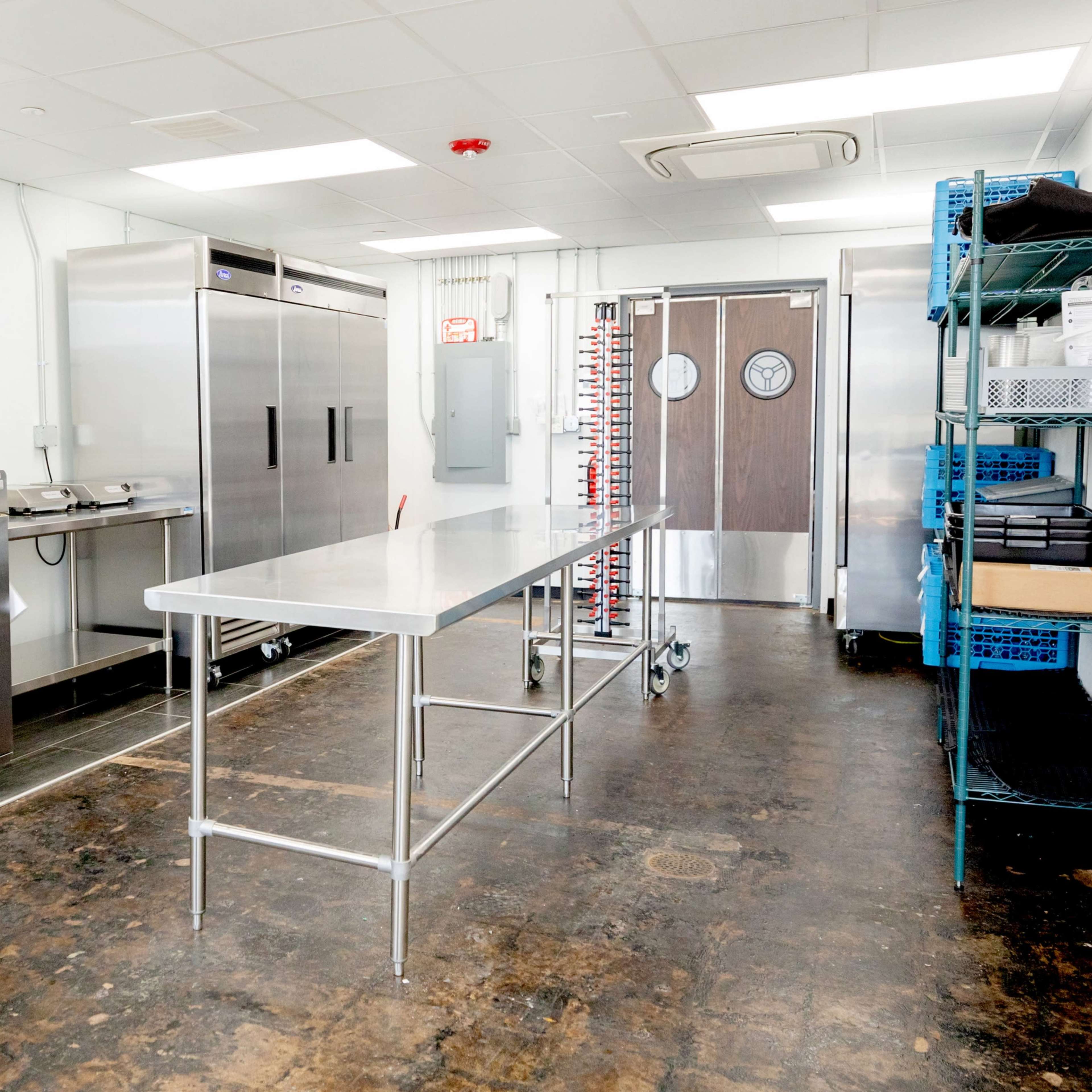 A modern commercial kitchen with stainless steel appliances, including refrigerated units and a central work table.