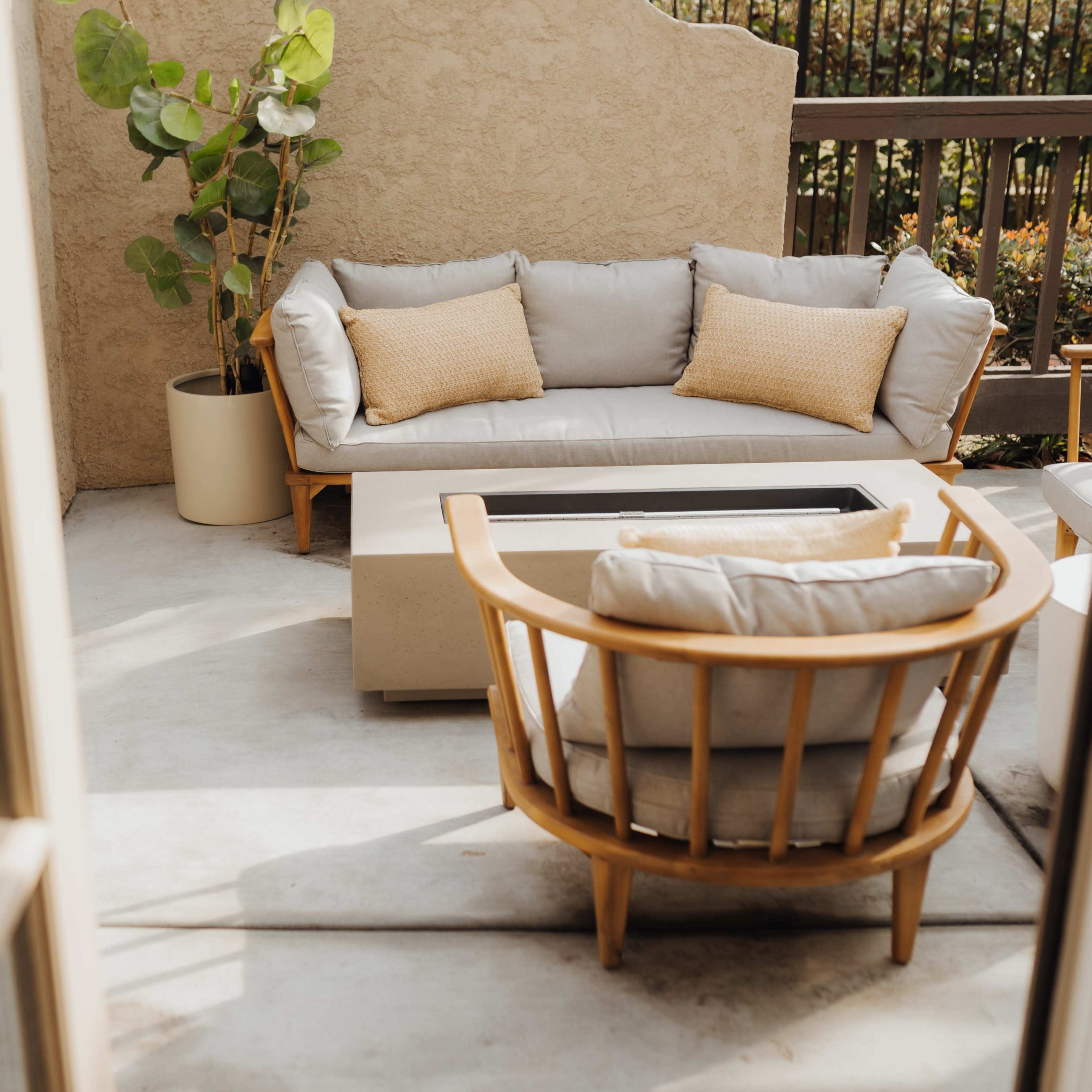 A cozy outdoor seating area features a gray sofa with cushions and a round wooden chair, accompanied by a potted plant.