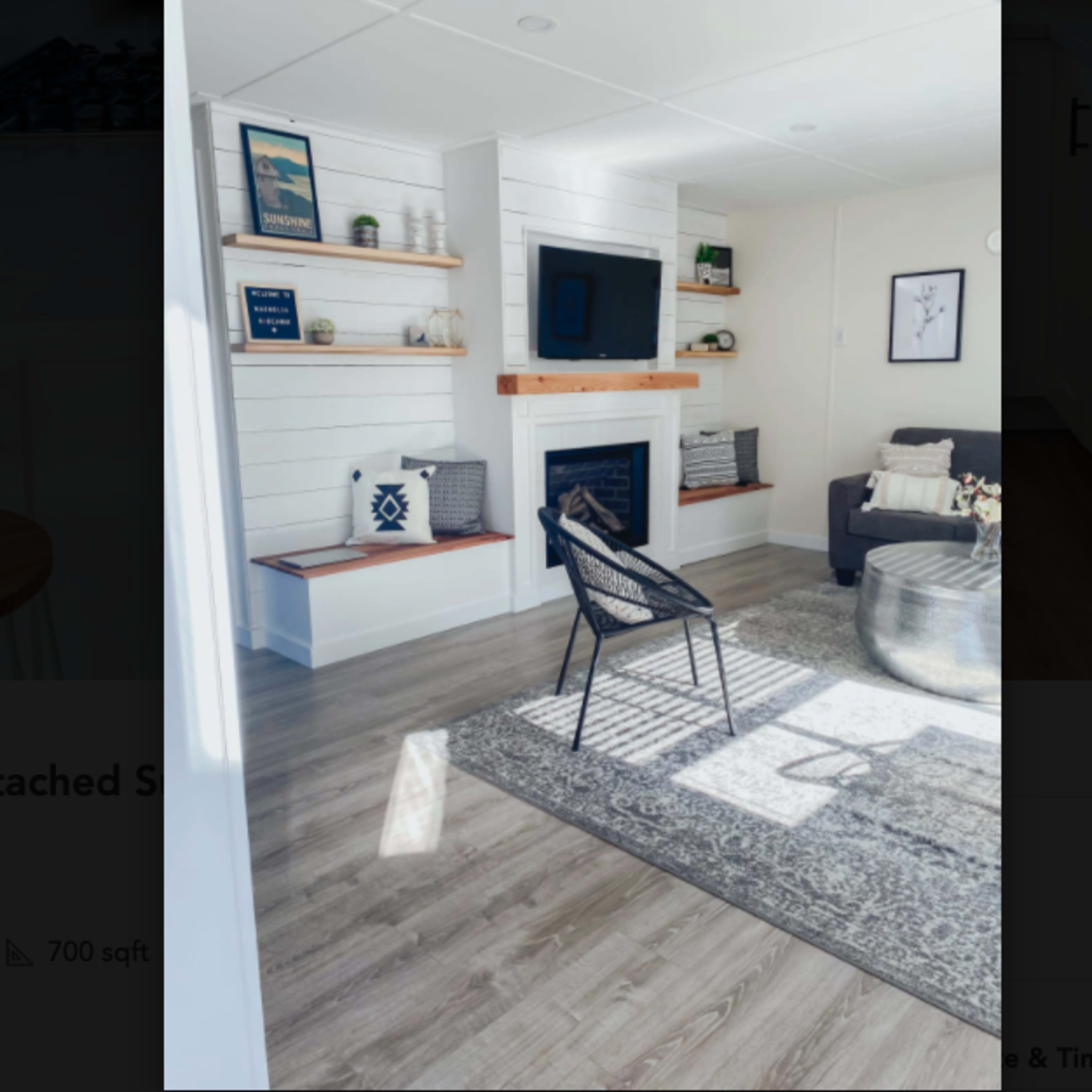 A modern room with a fireplace, wall shelves, a gray sofa, and a decorative rug on the floor.