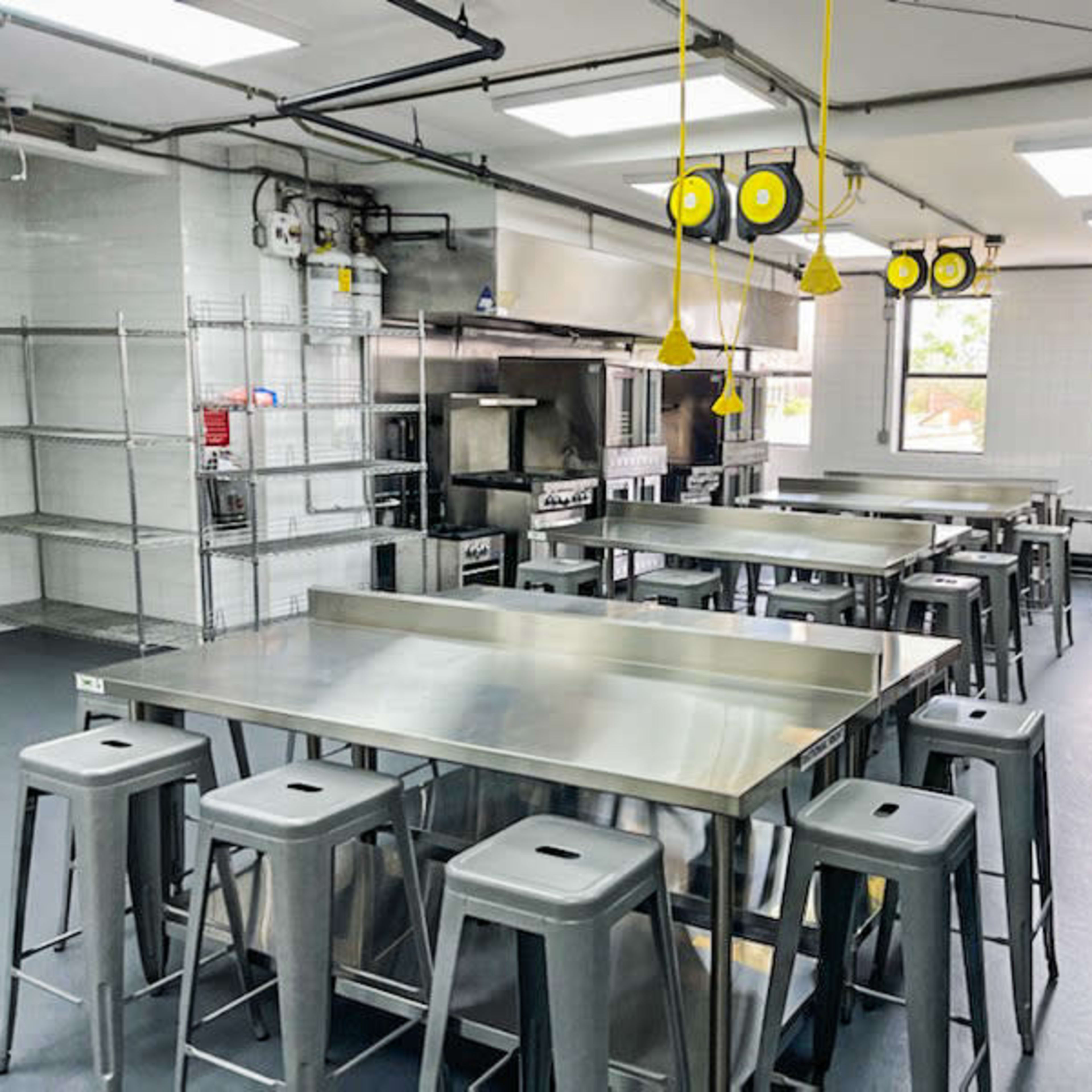 A spacious commercial kitchen equipped with stainless steel tables, metal stools, and industrial appliances.