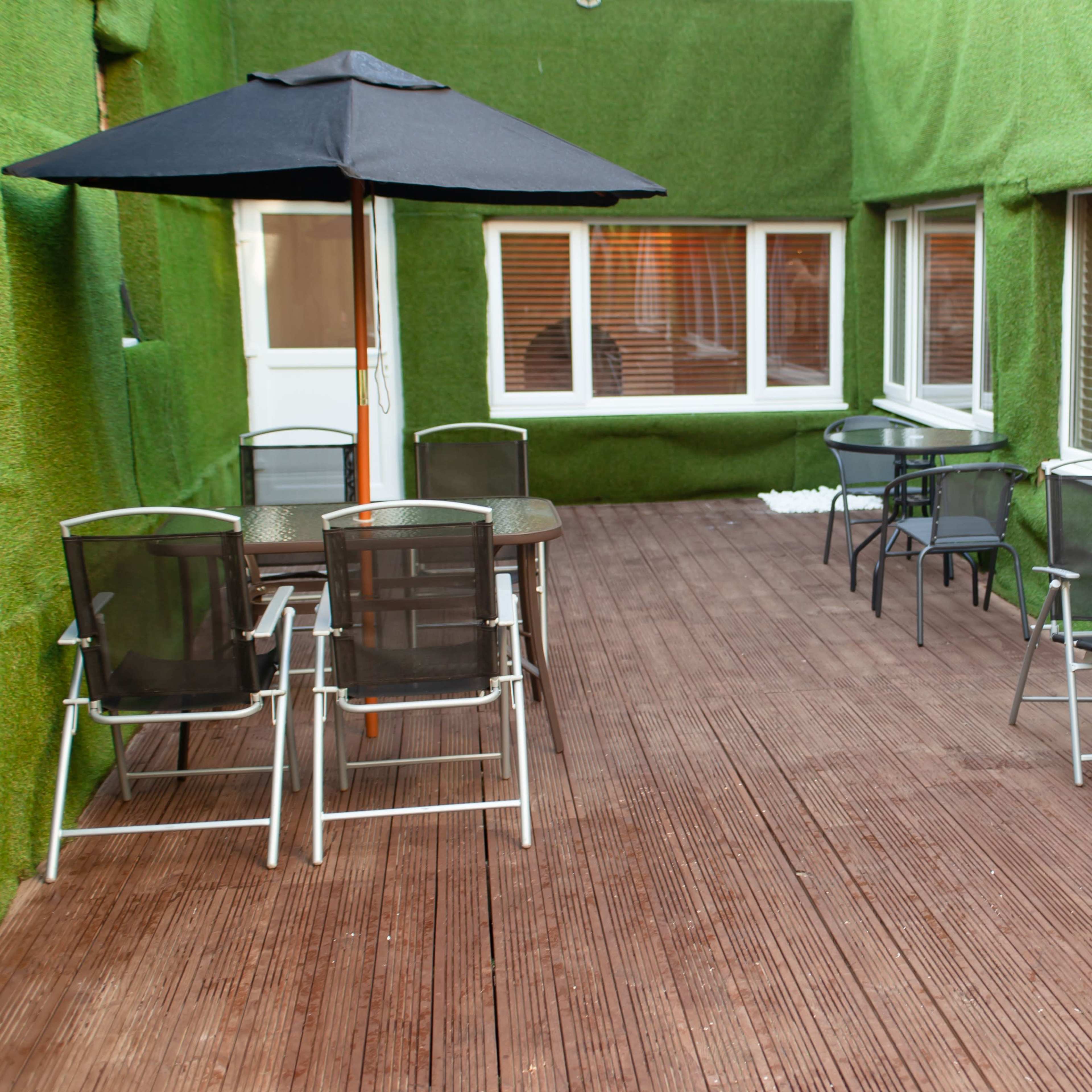 A deck area with several tables and chairs, surrounded by green synthetic grass-covered walls, and a black umbrella over one of the tables.