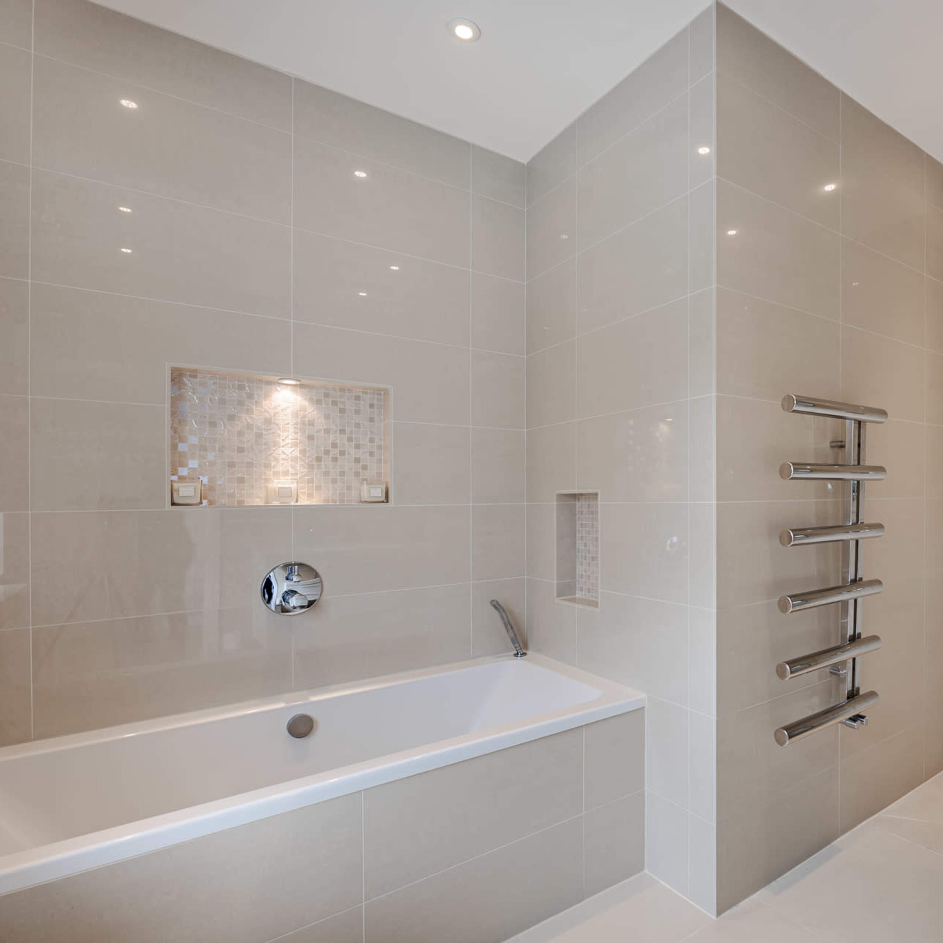 A modern bathroom featuring a bathtub on one side, a double sink counter, and a vertical towel warmer against tiled walls.