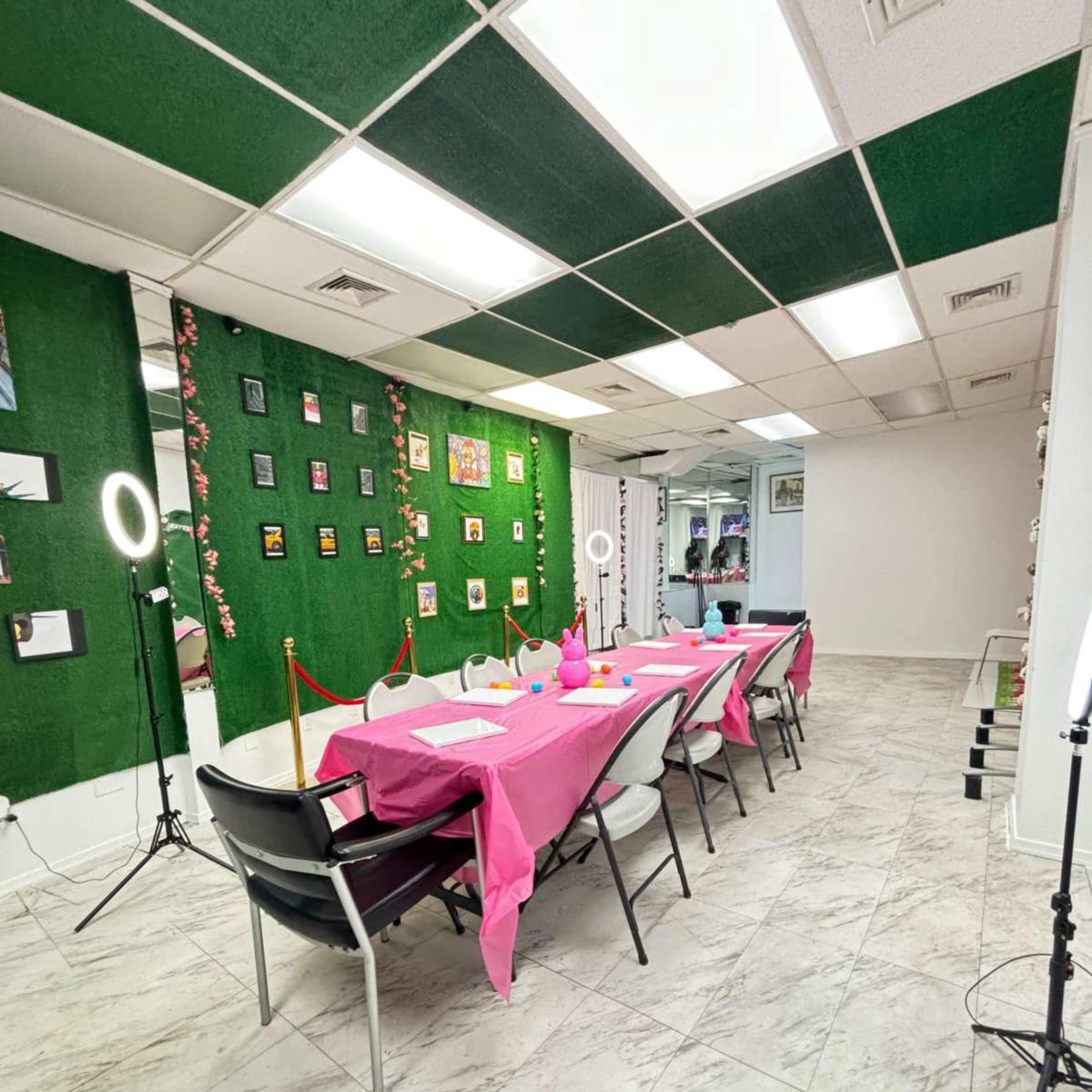 A long table covered with a pink cloth is set up in a brightly lit room, surrounded by decorations on the walls and lighting equipment.