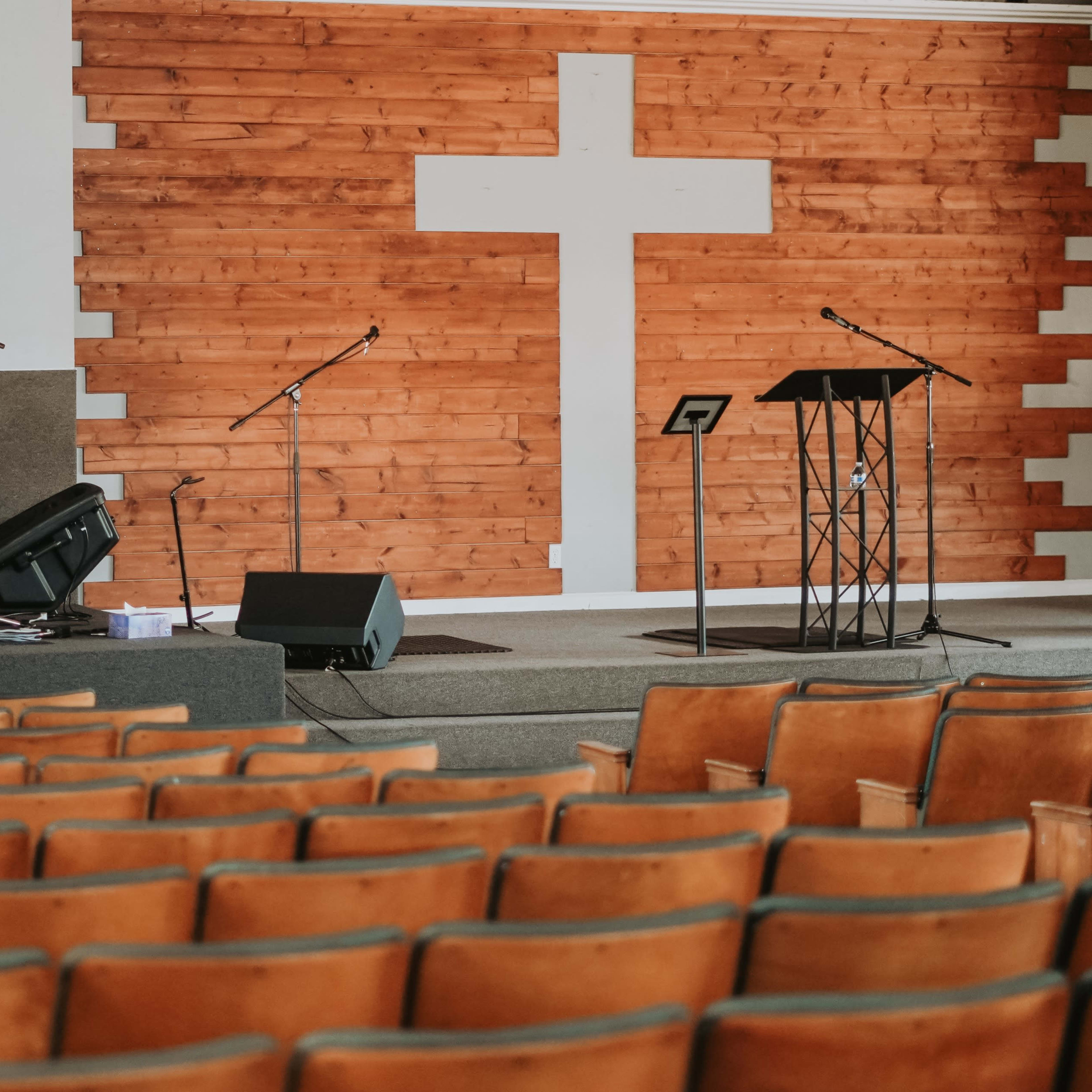 A church interior with a wooden cross on the wall, a stage set for a service featuring a drum set, microphones, and a podium.