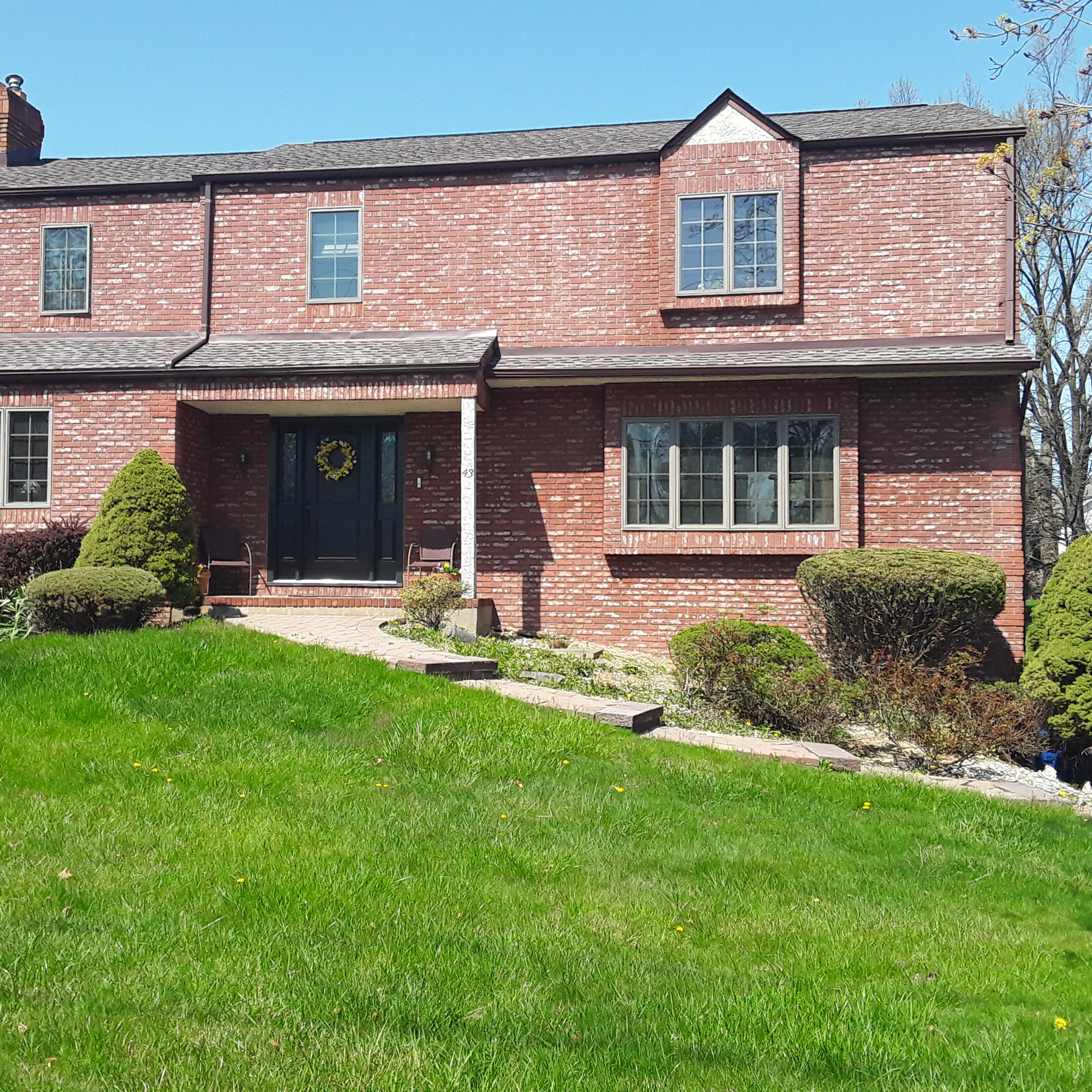 A two-story brick house with a landscaped front yard and a pathway leading to the entrance.
