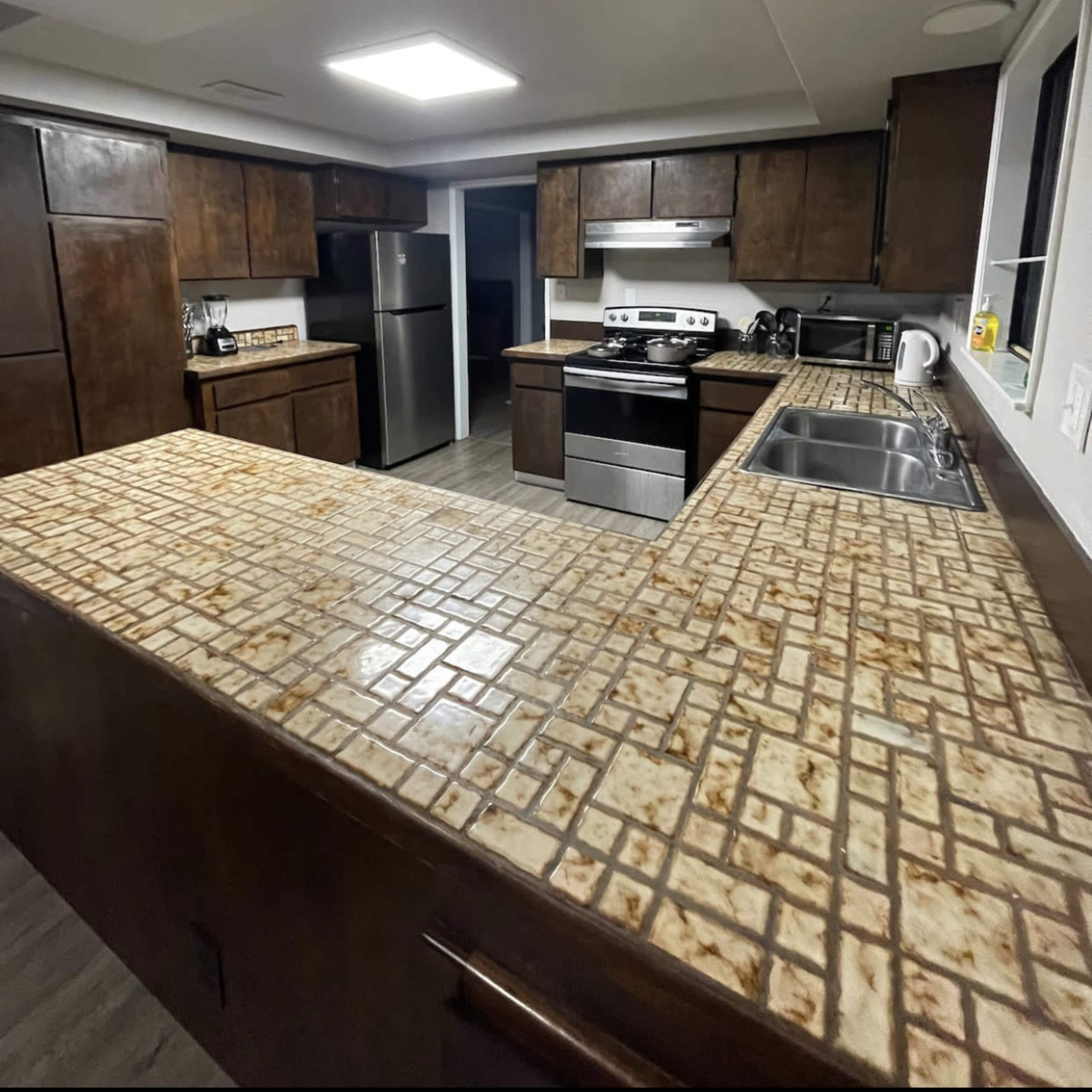 A kitchen with dark wooden cabinets, a stainless steel refrigerator, and a tiled countertop.