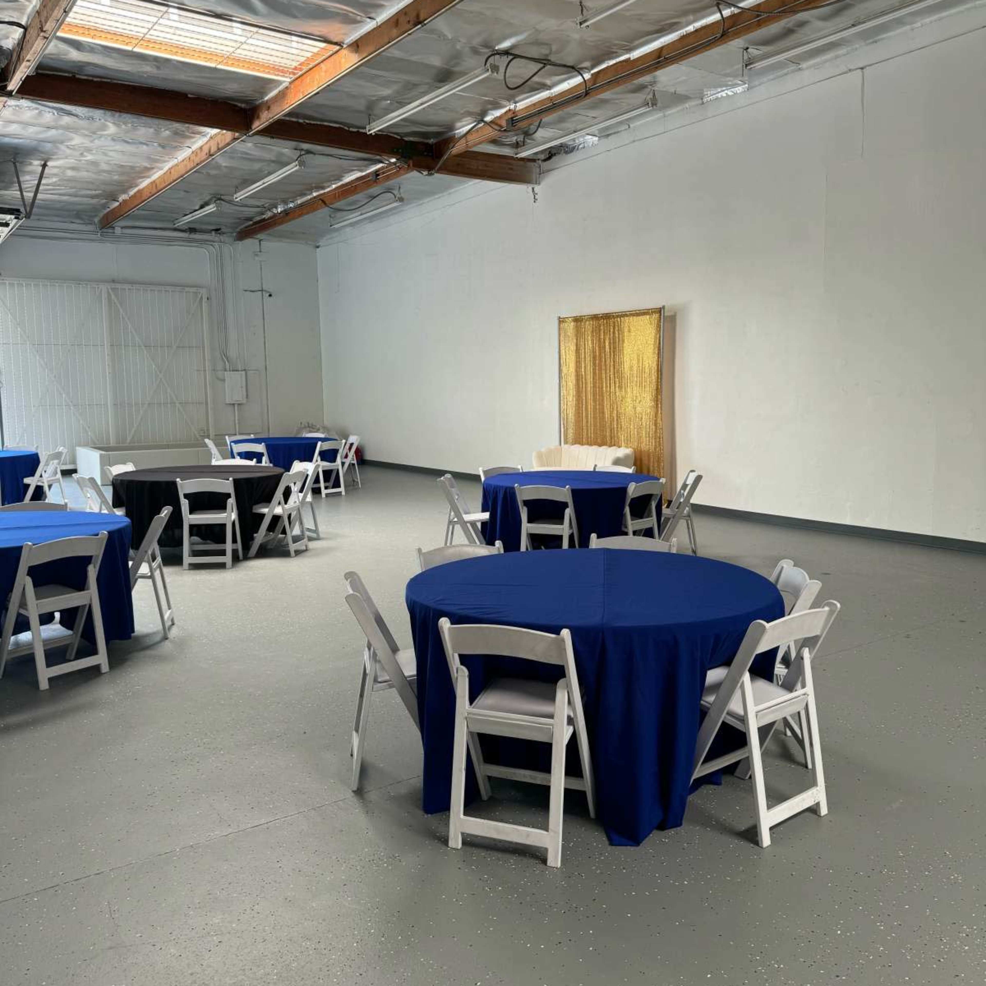 A spacious room with several round tables covered in blue tablecloths and white chairs arranged around them.
