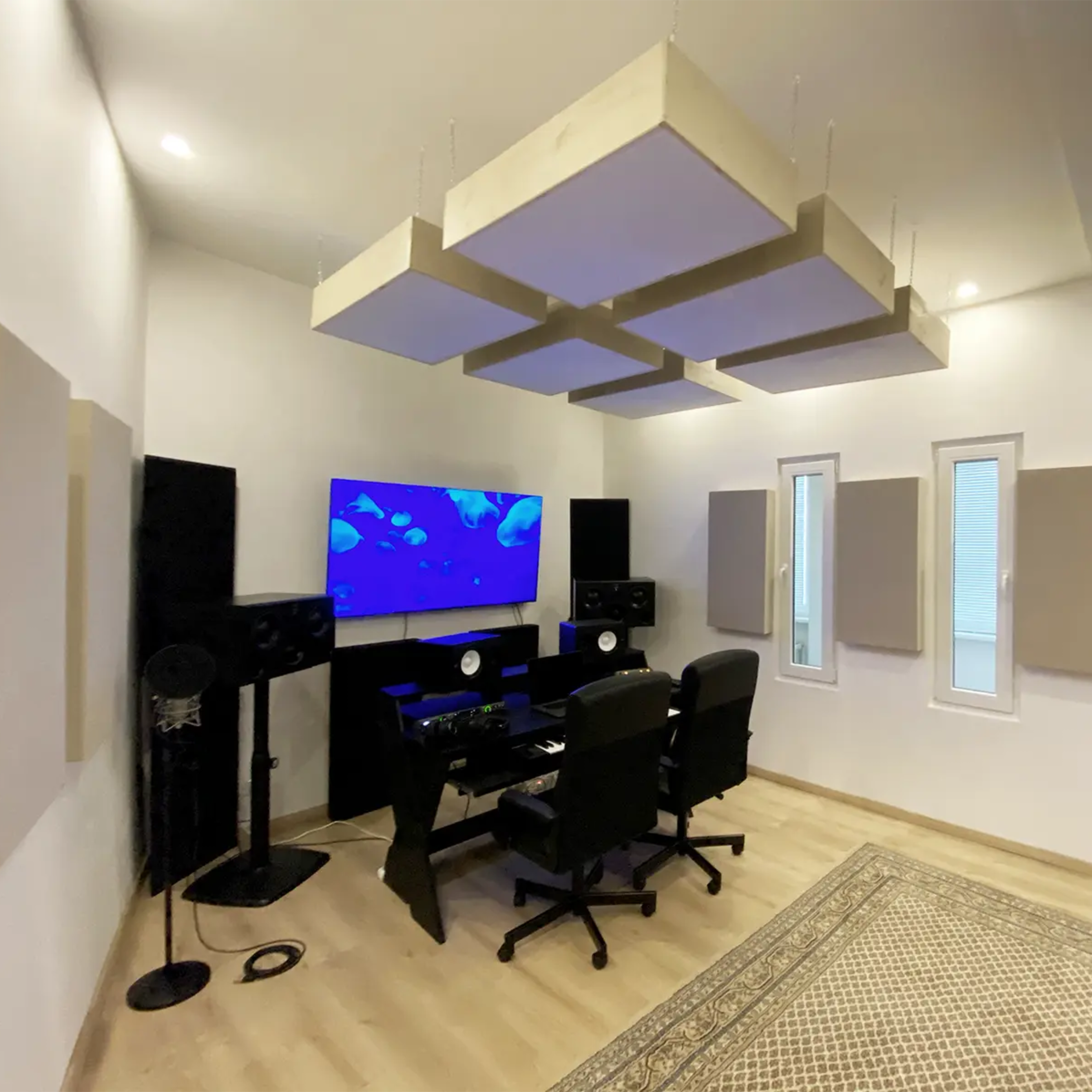 A modern recording studio with soundproofing panels, a mixing desk, two black chairs, and a large screen displaying a blue underwater scene.