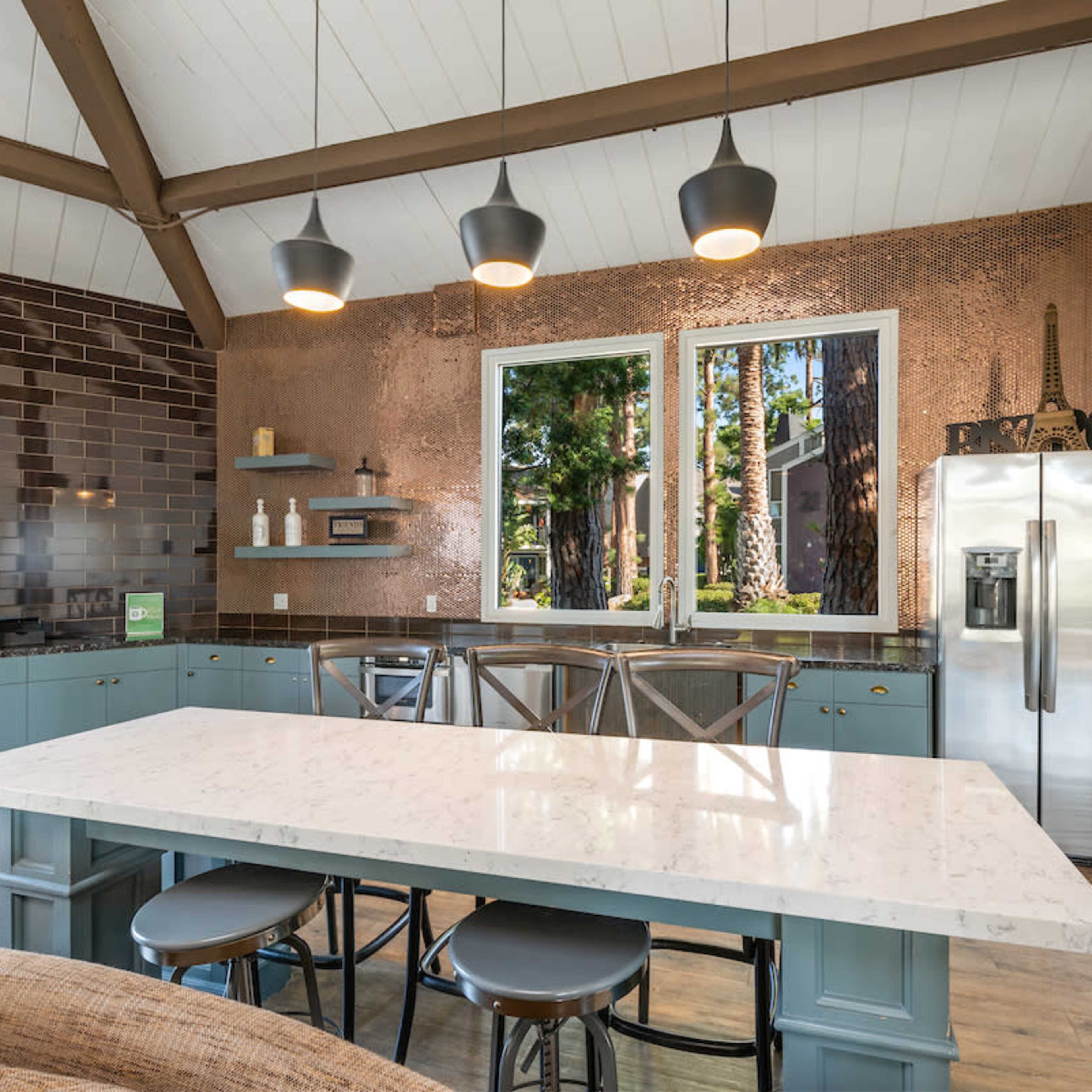 A modern kitchen with a large marble island, copper accent walls, and large windows overlooking a forested area.