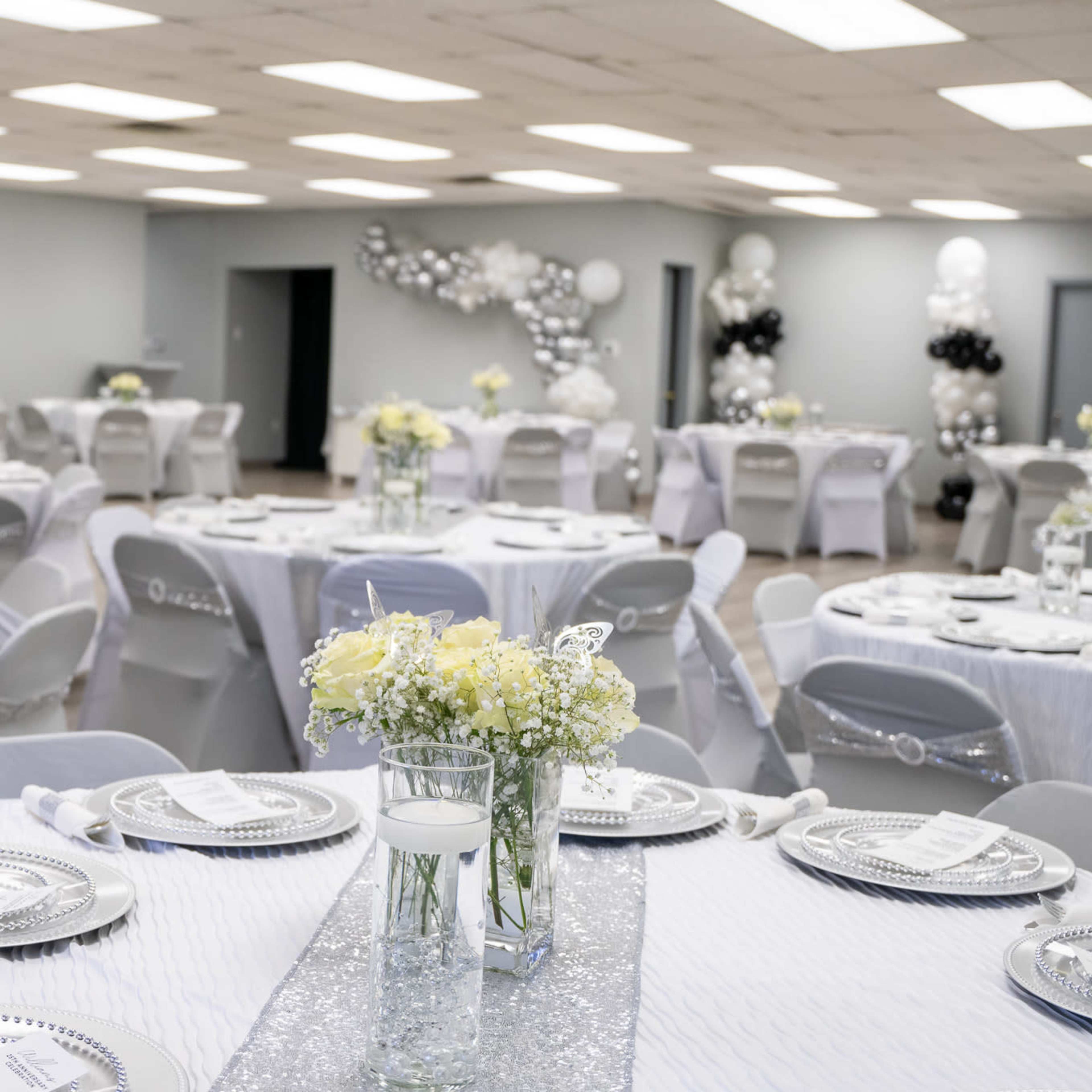 A banquet hall set up for an event, featuring round tables covered with white tablecloths, adorned with floral centerpieces and shining tableware.