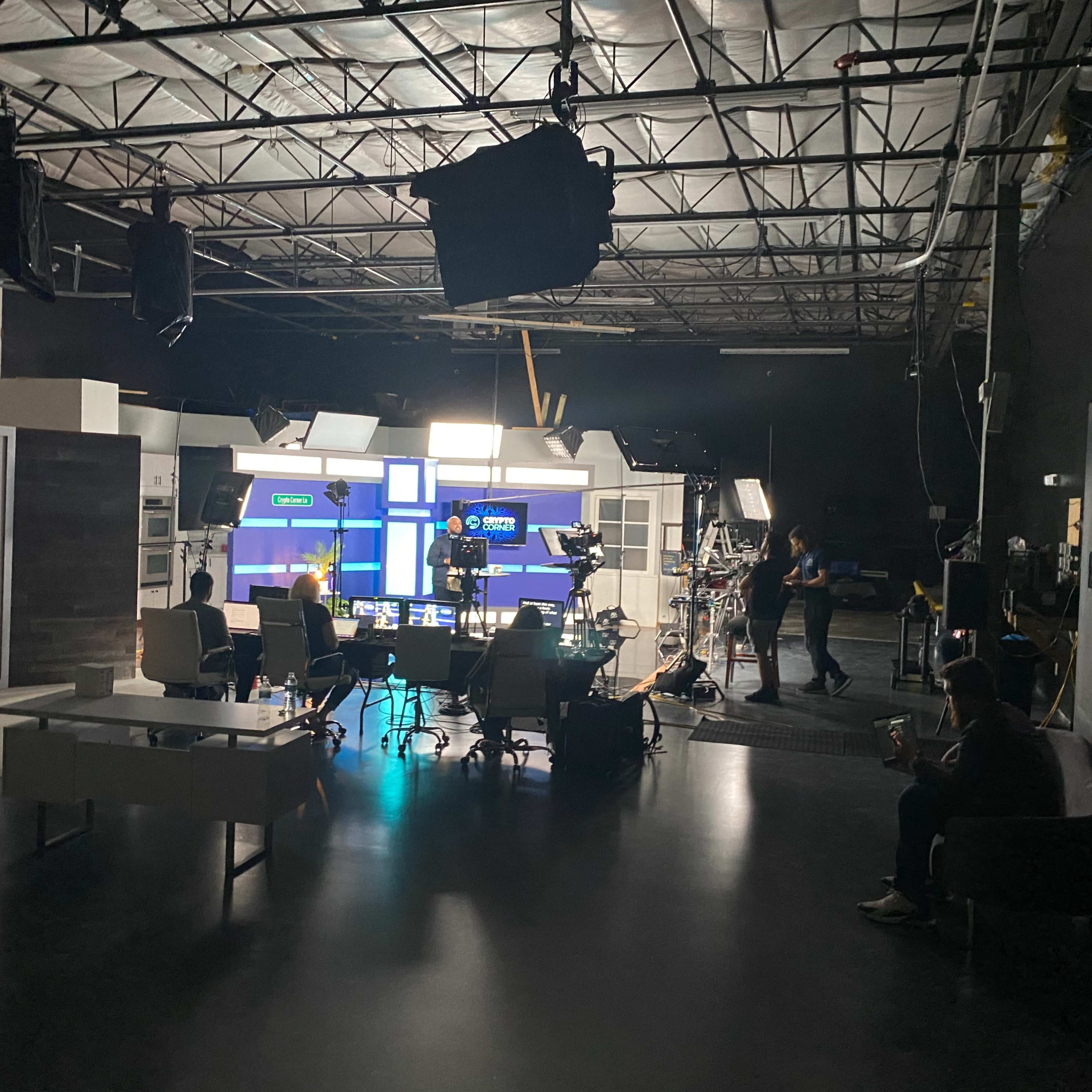 A television studio set is prepared for filming, with cameras, lighting equipment, and various pieces of furniture arranged in the space.