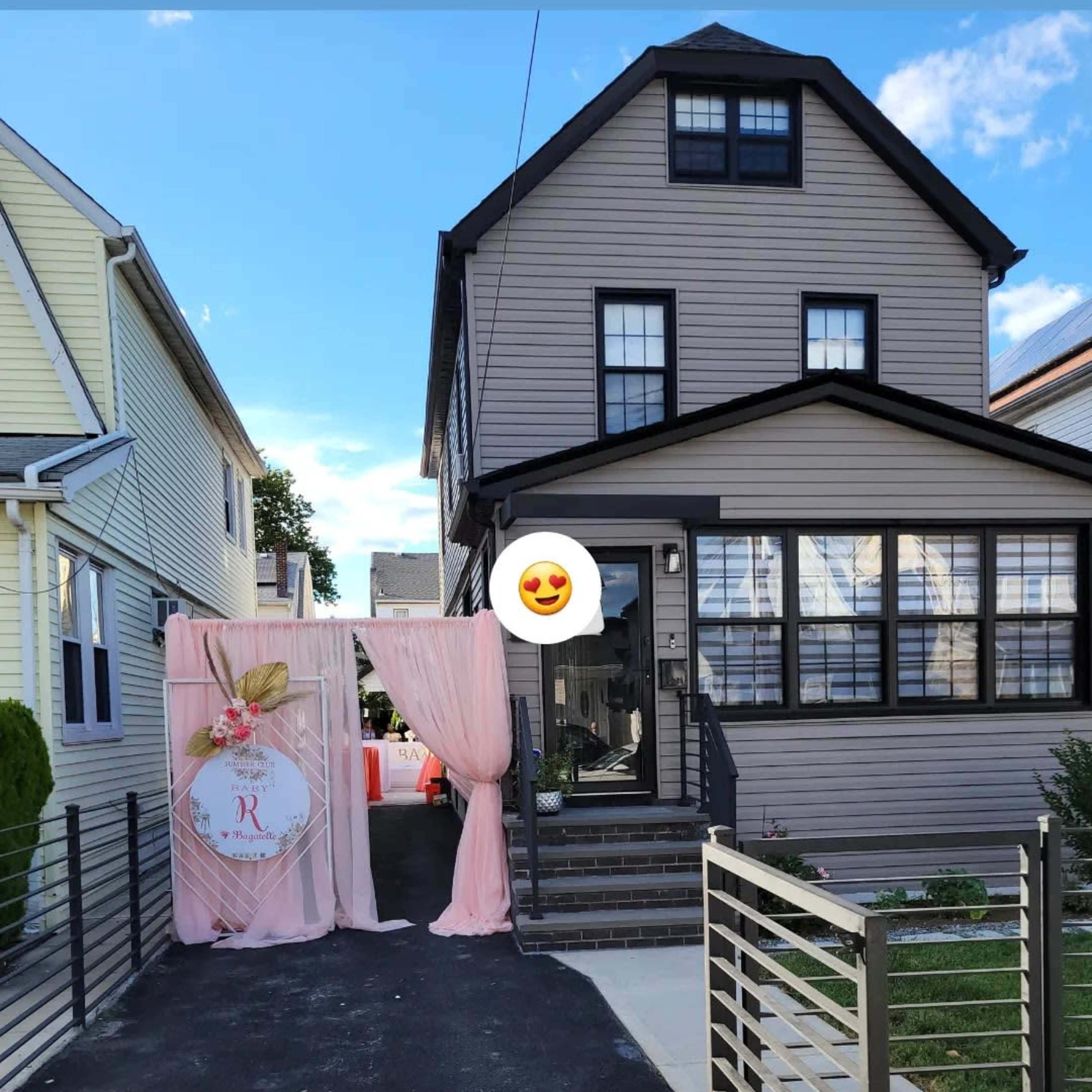 A two-story house with black windows and a front porch is adjacent to a decorative entryway draped in pink fabric.