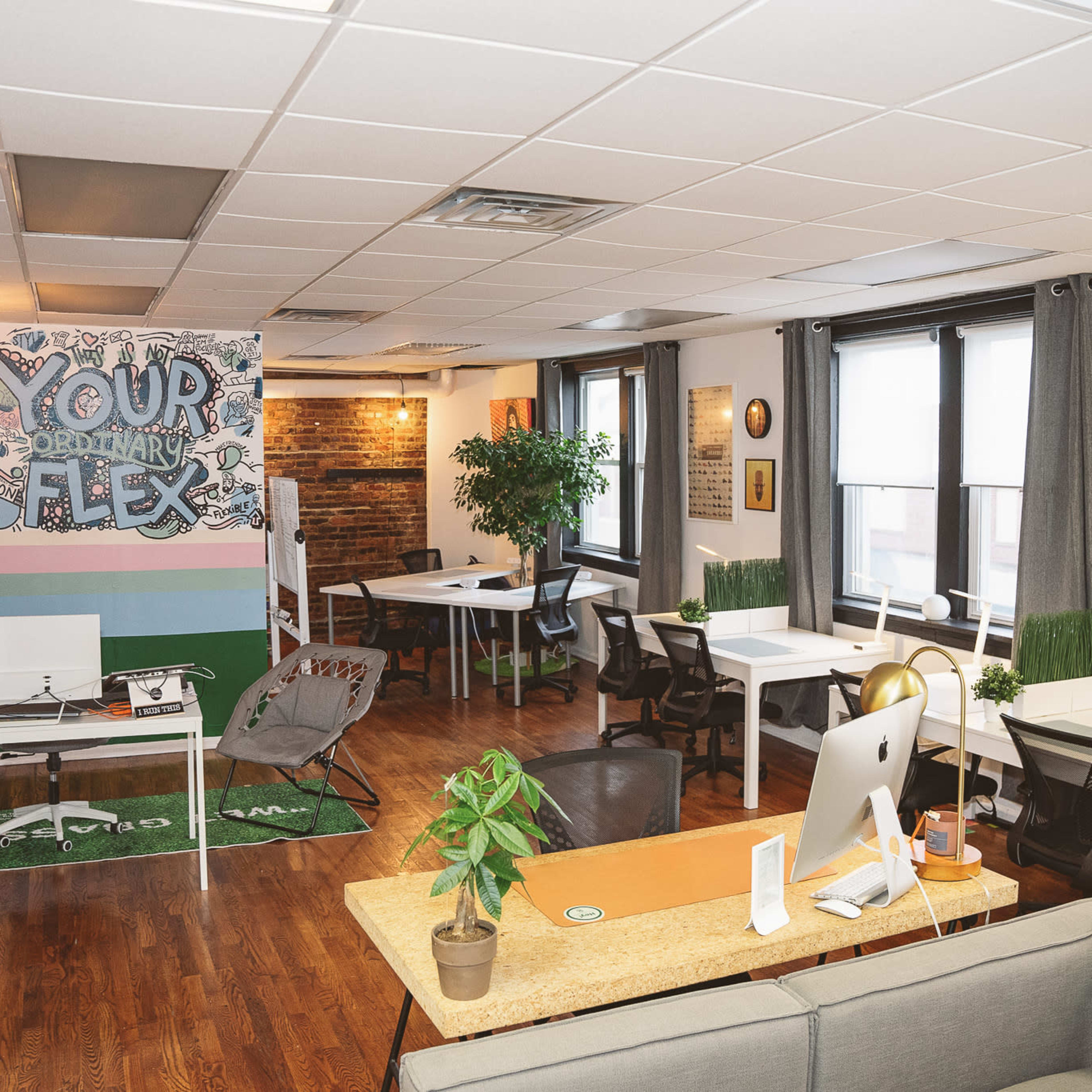 A modern office space features a mix of workstations, a communal area, and vibrant wall art in a well-lit setting.
