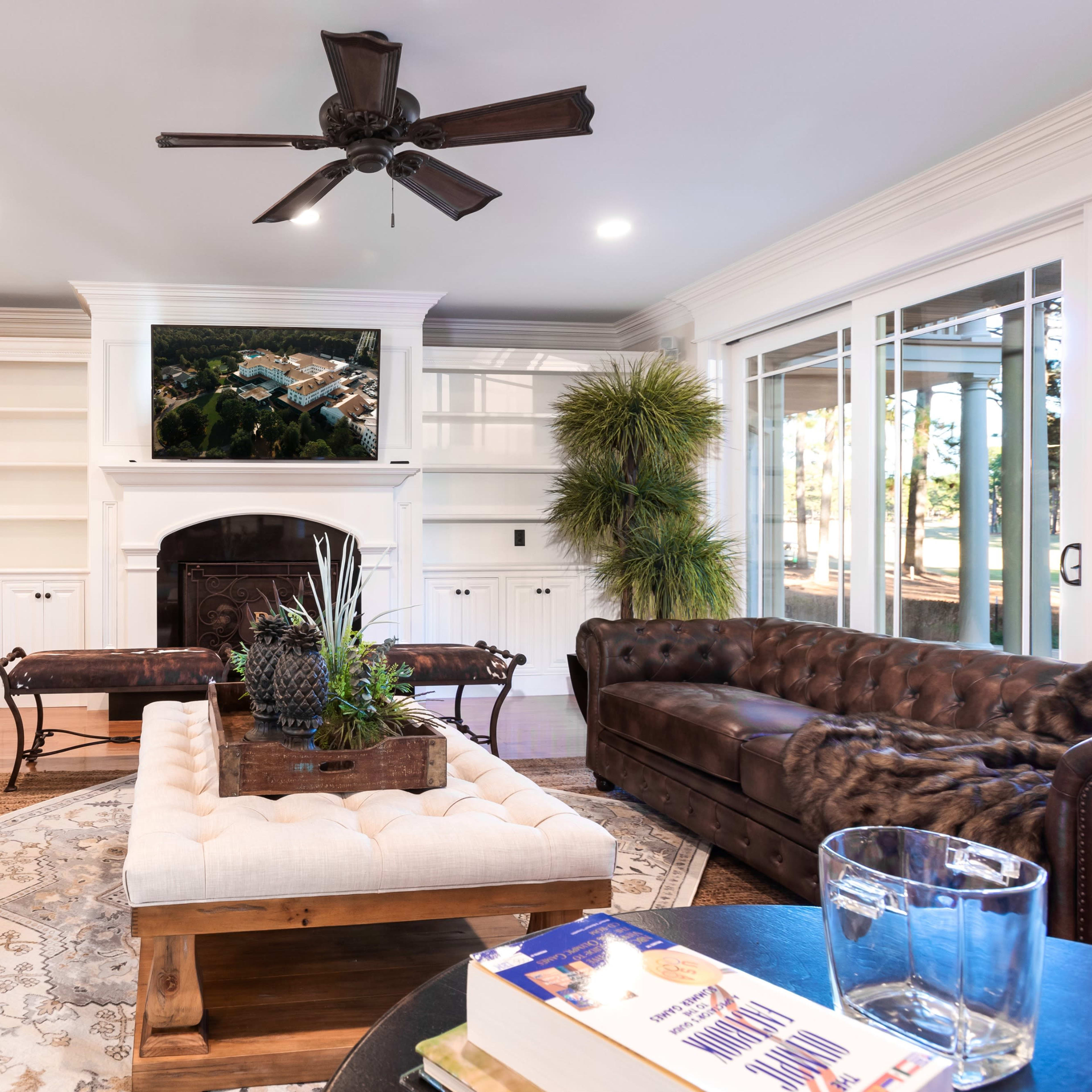A comfortable living room features two brown leather sofas, a wooden coffee table with a plant centerpiece, and a fireplace with a television mounted above.