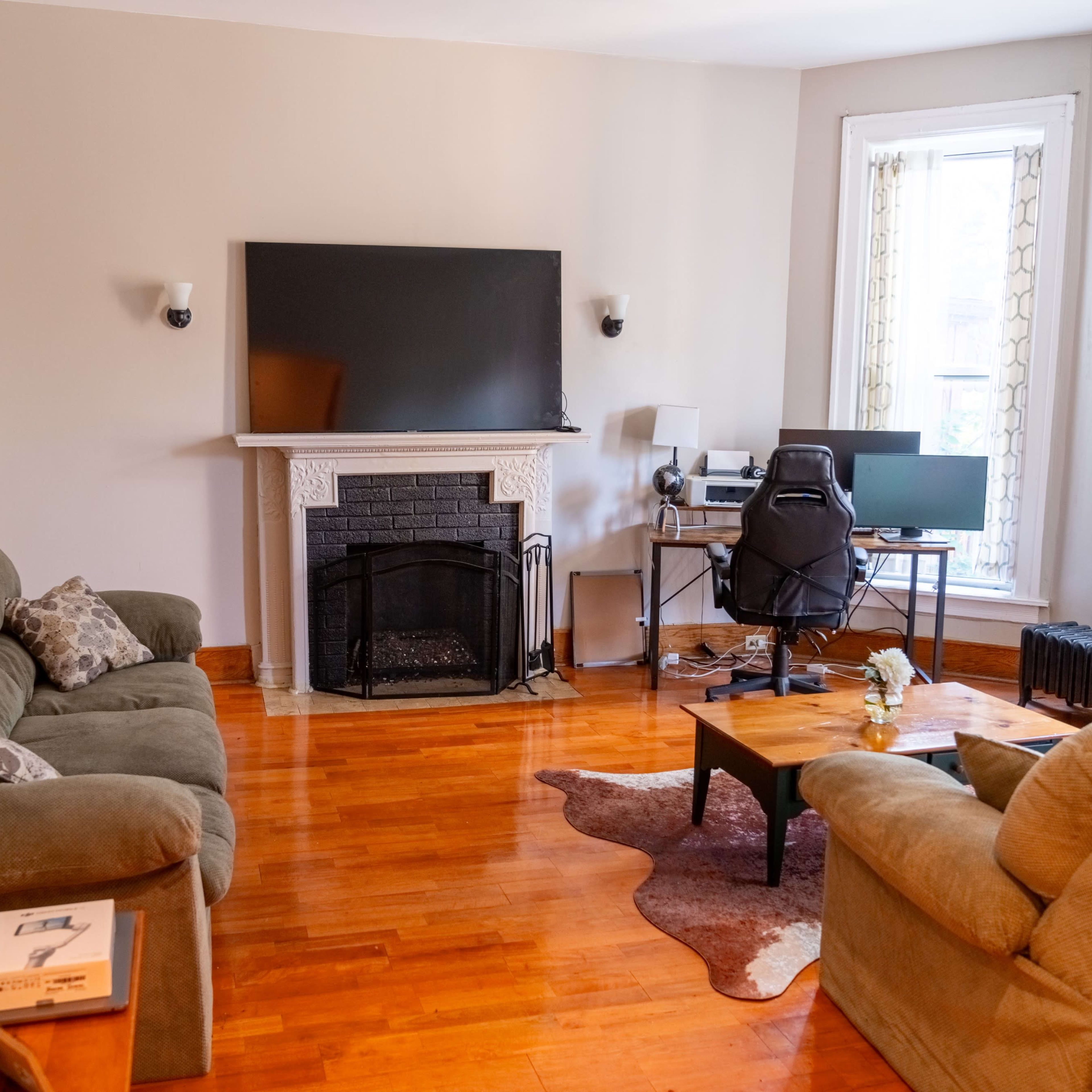 A living room with a television mounted above a fireplace, two couches, a coffee table, and a computer setup in a corner.