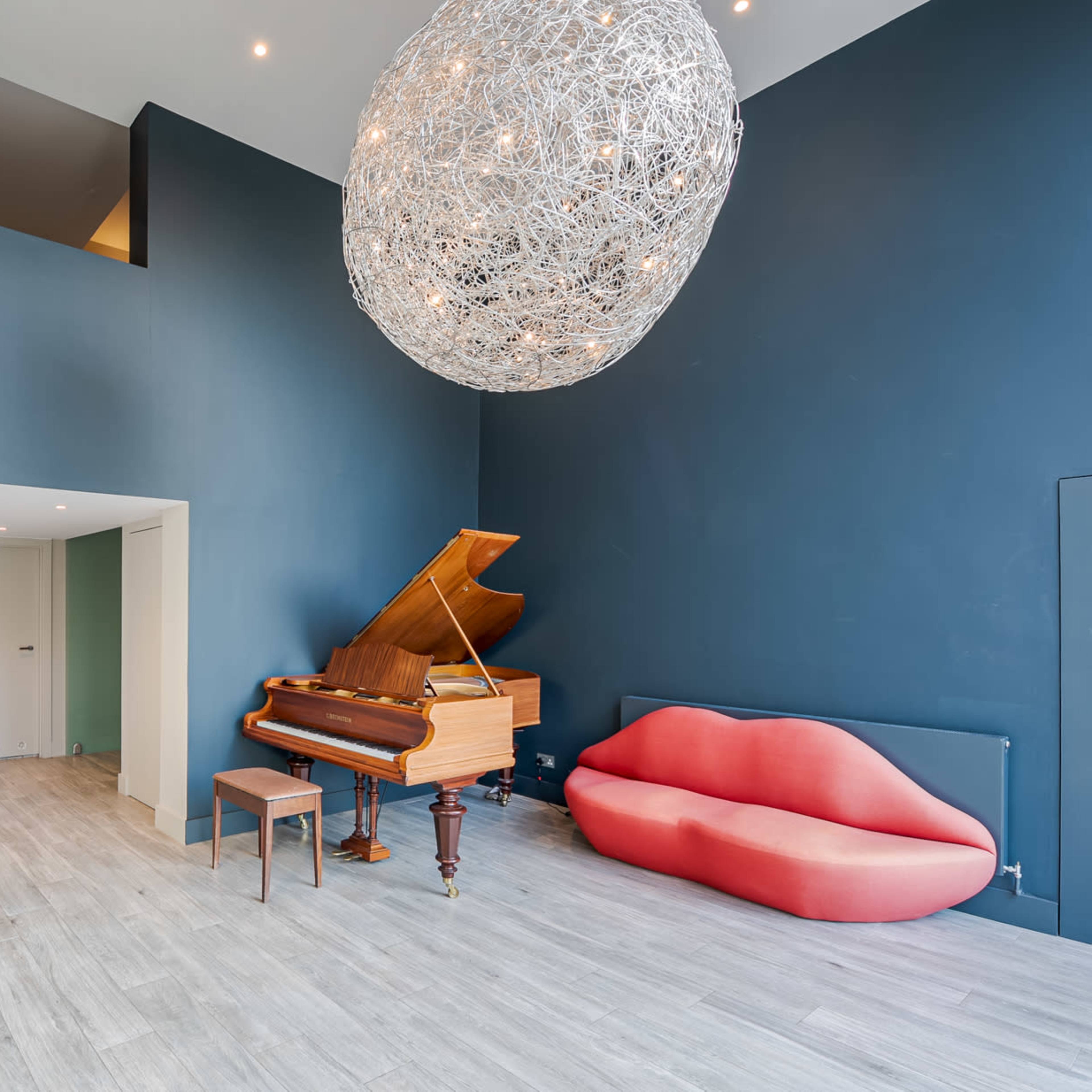 A spacious room featuring a grand piano, a red modern sofa, and a large decorative light fixture hanging from the ceiling.