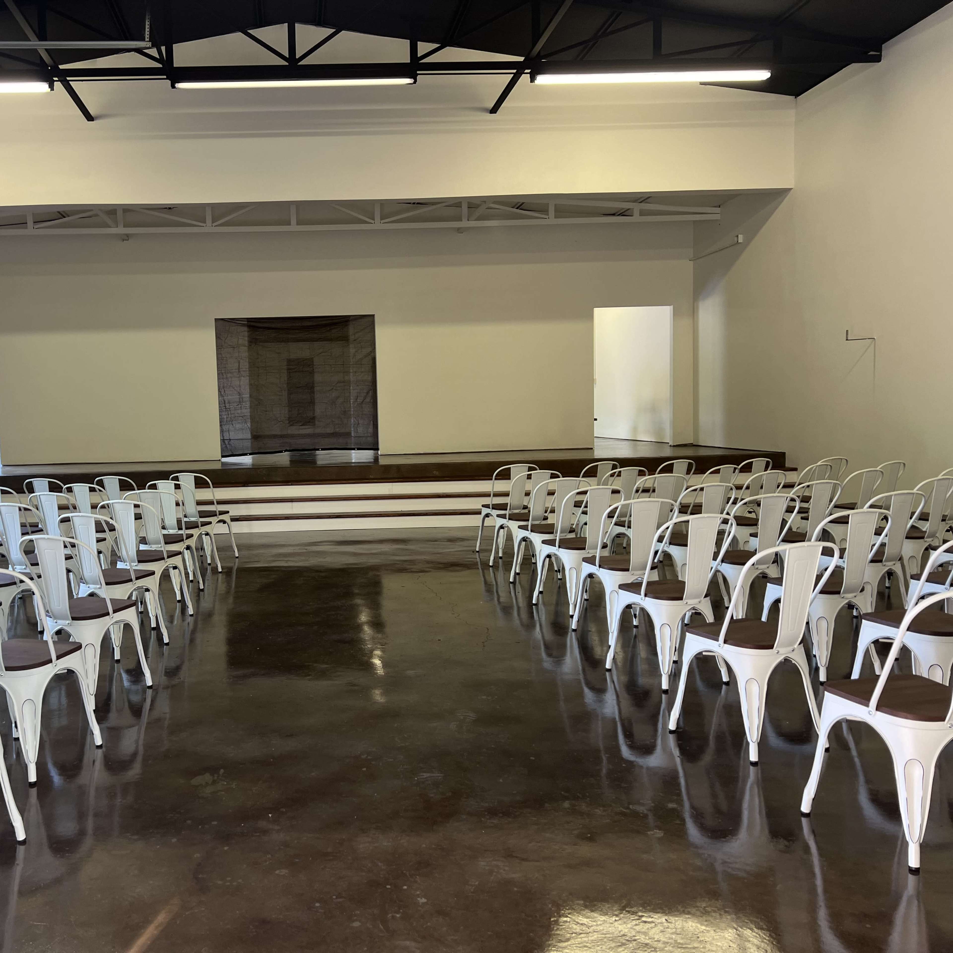 A spacious room with metal chairs arranged in rows facing a stage at the front.