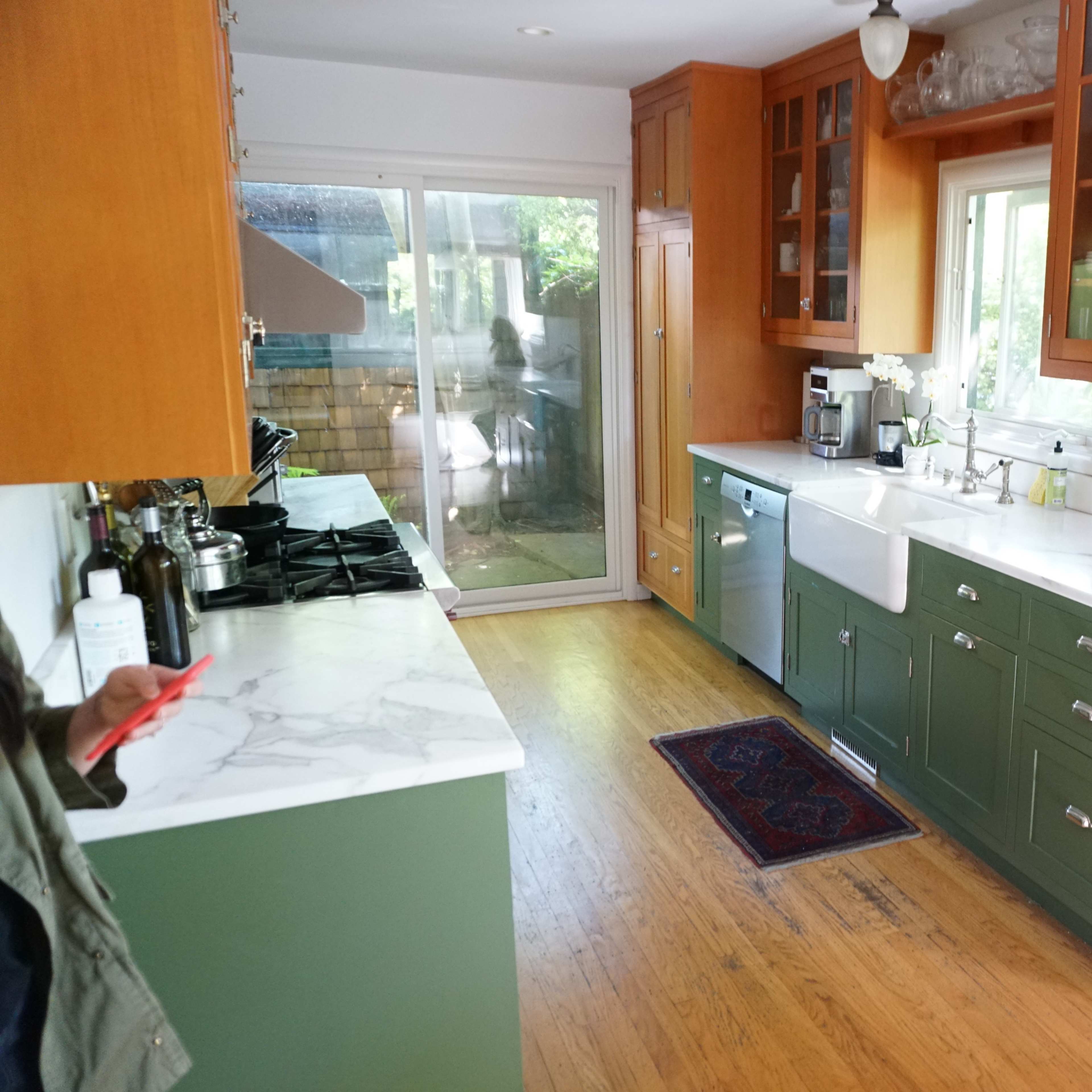 A kitchen with green cabinets, white countertops, and wooden flooring, featuring a sink, a stove, and a dining table.