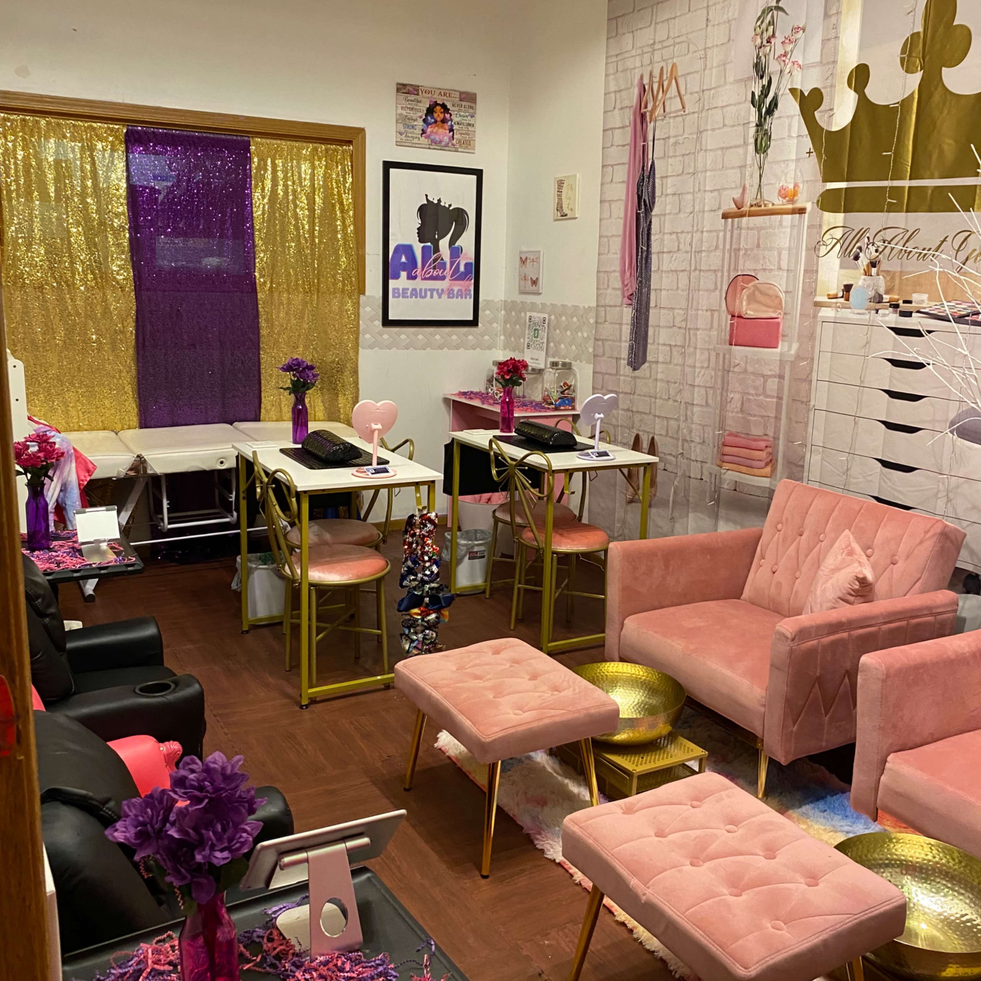 A brightly decorated beauty salon featuring pink furniture, gold accents, and a colorful backdrop with a sparkling curtain.