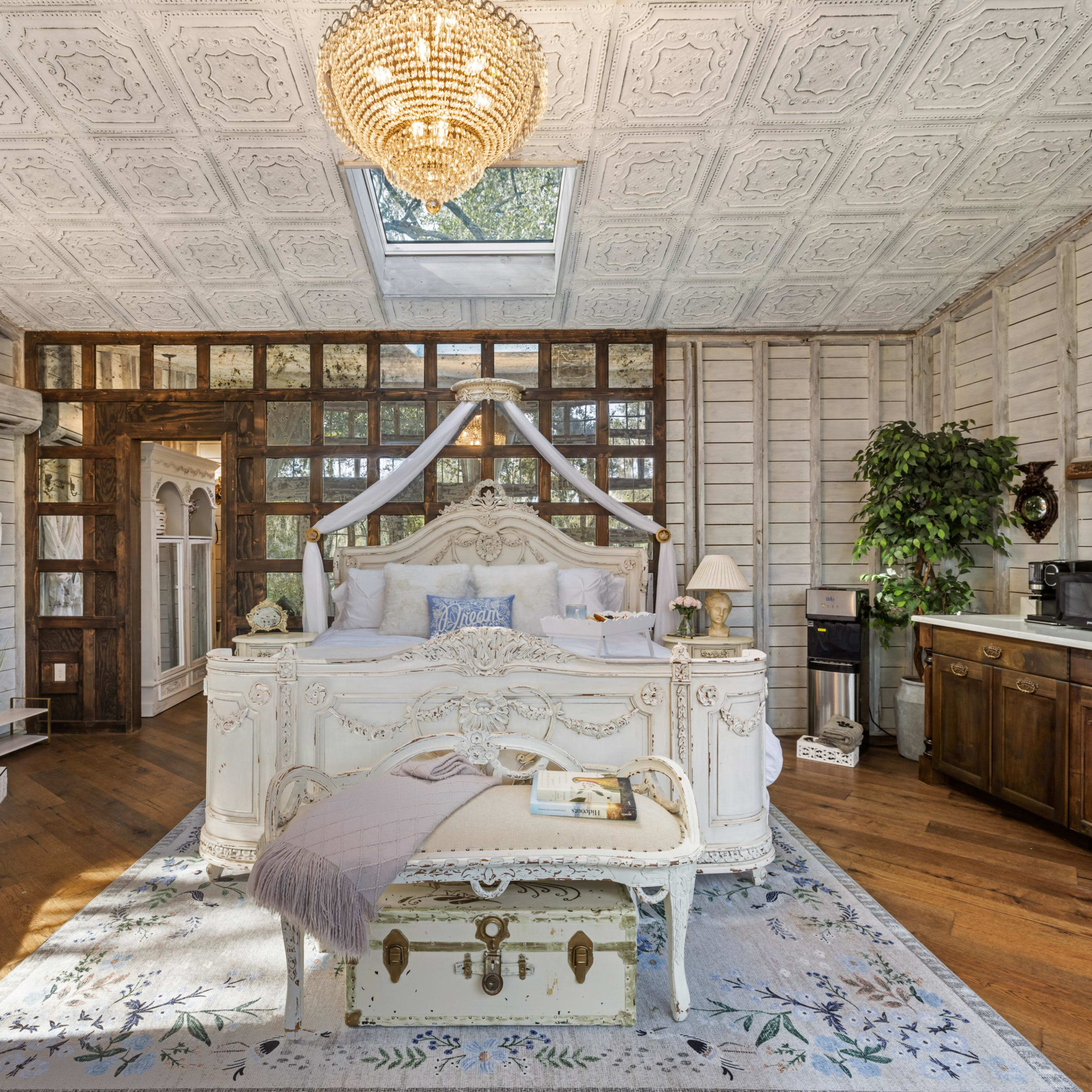 A vintage-style bedroom featuring a large white bed, a wooden bathtub, and a mix of rustic and elegant furnishings.