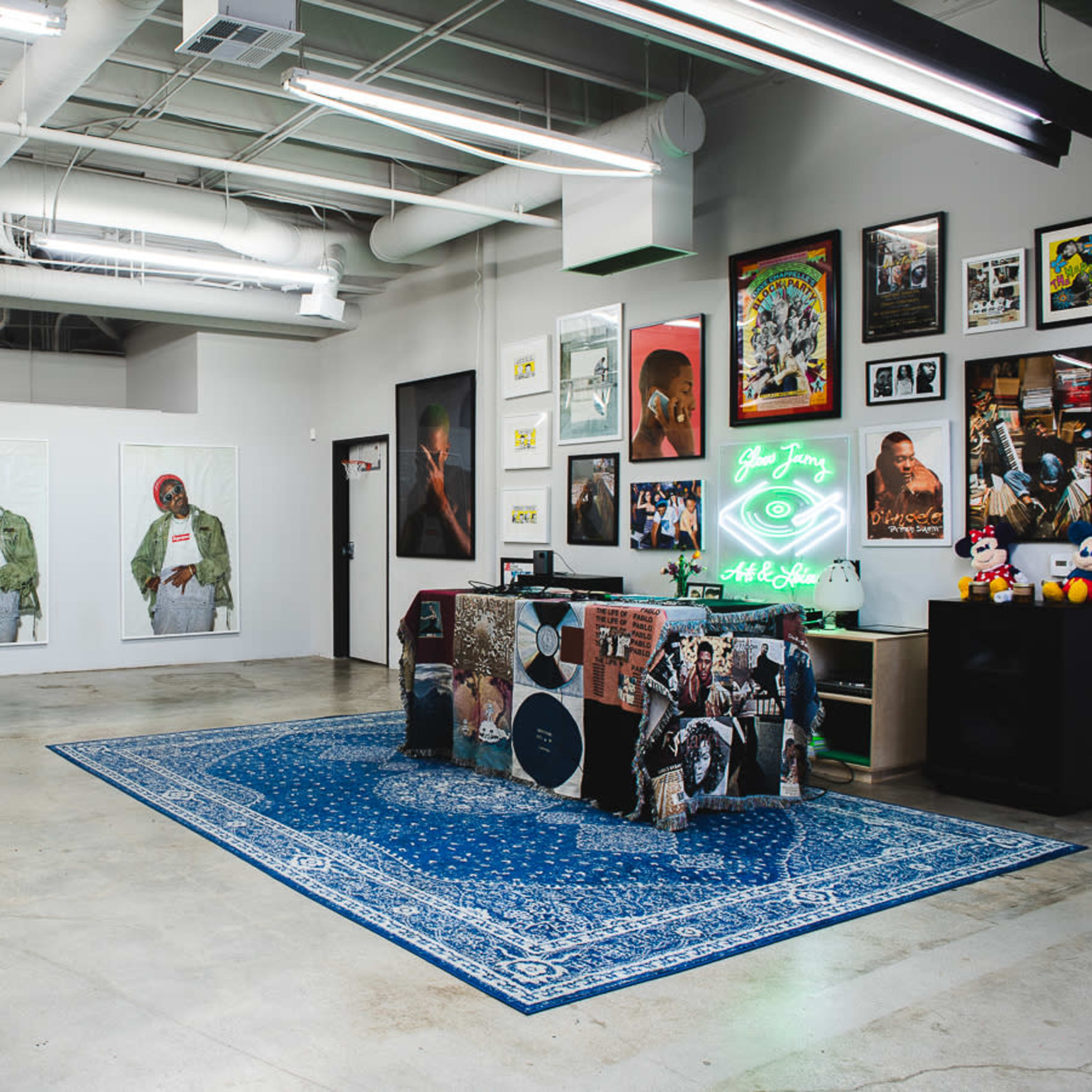 An art gallery with large framed artworks on white walls, a decorated reception desk, and various framed posters and photographs arranged around the space.