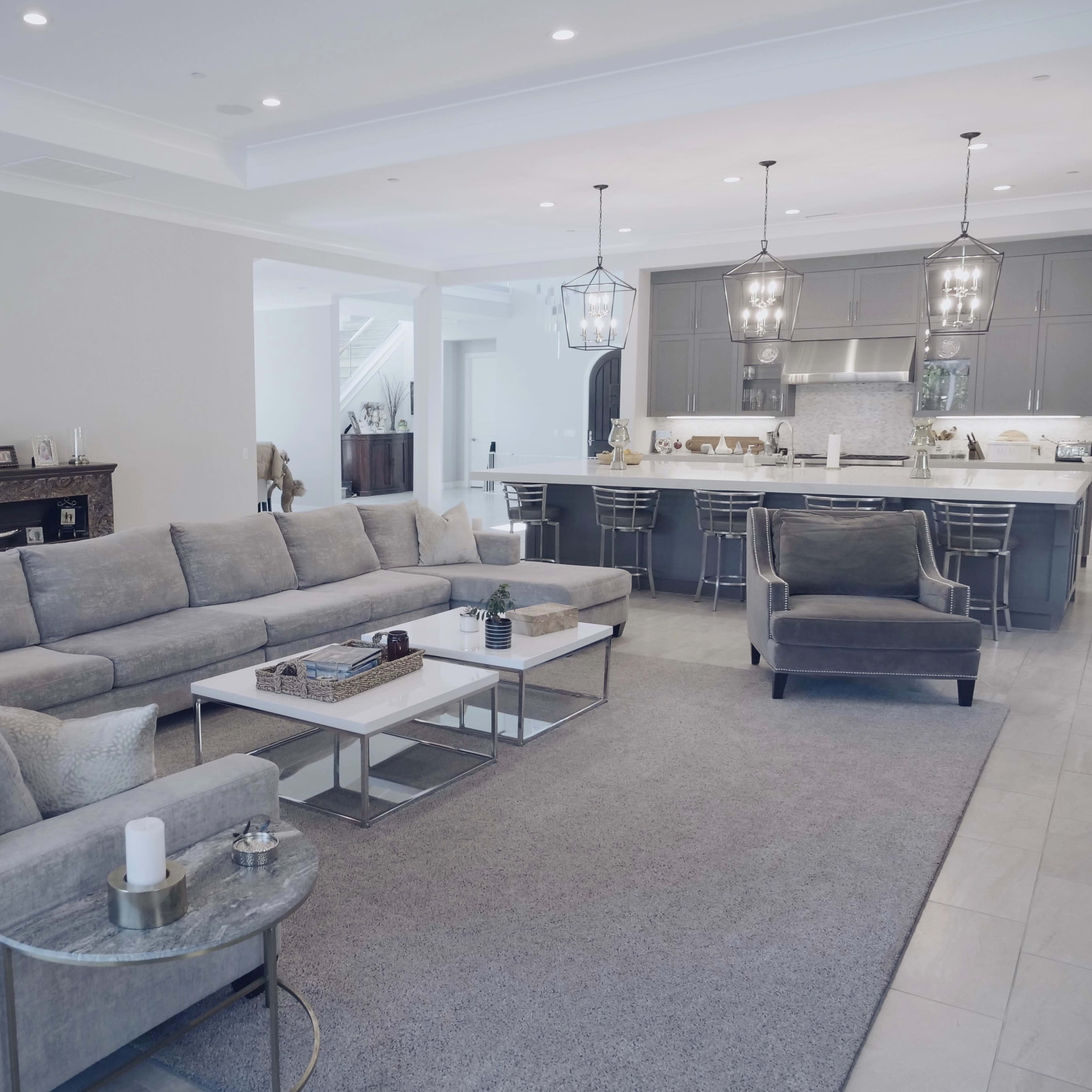 A spacious living room features a large gray sectional sofa, a matching chair, and a modern kitchen visible in the background.