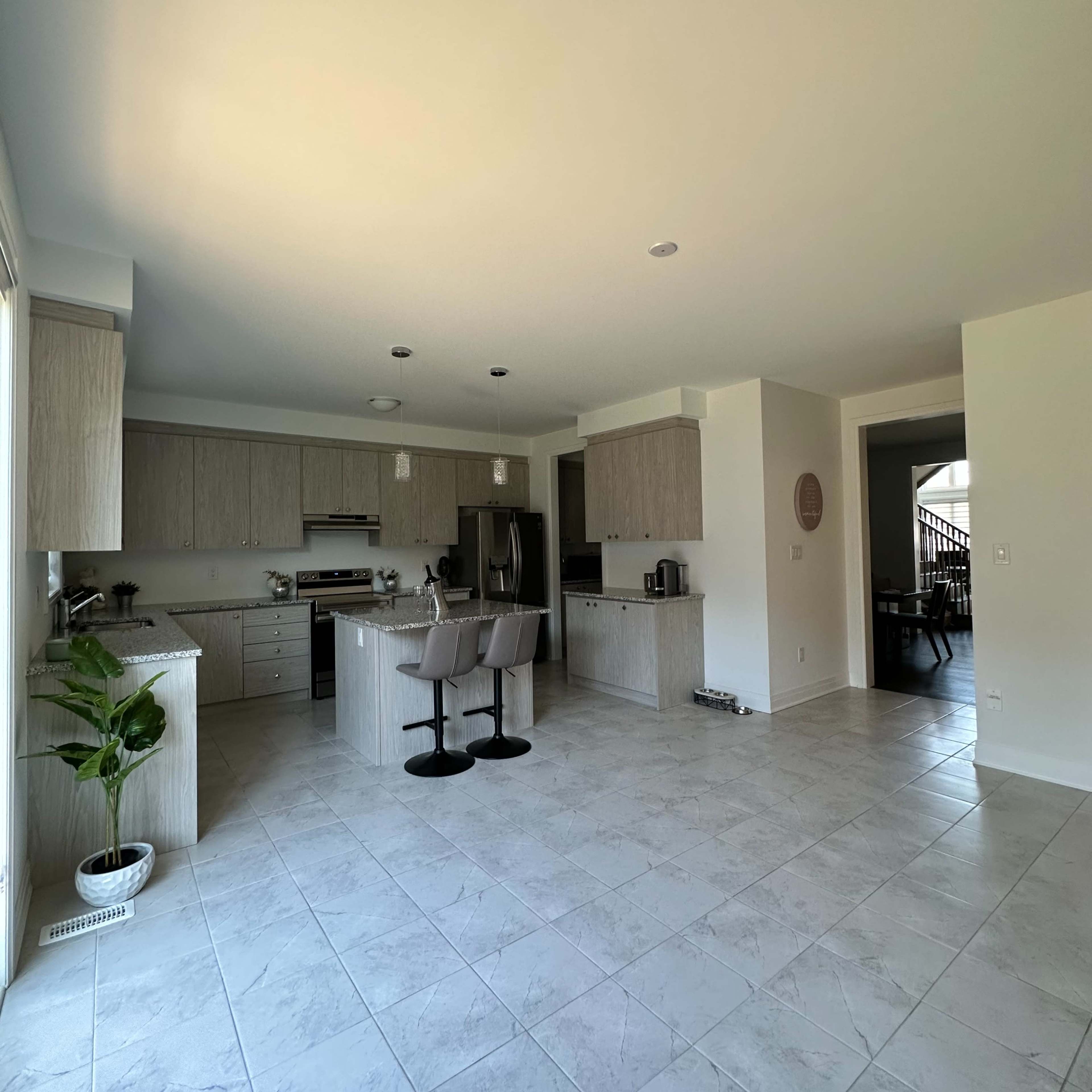 A modern kitchen with light-colored cabinetry, a central island with two stools, and tiled flooring.