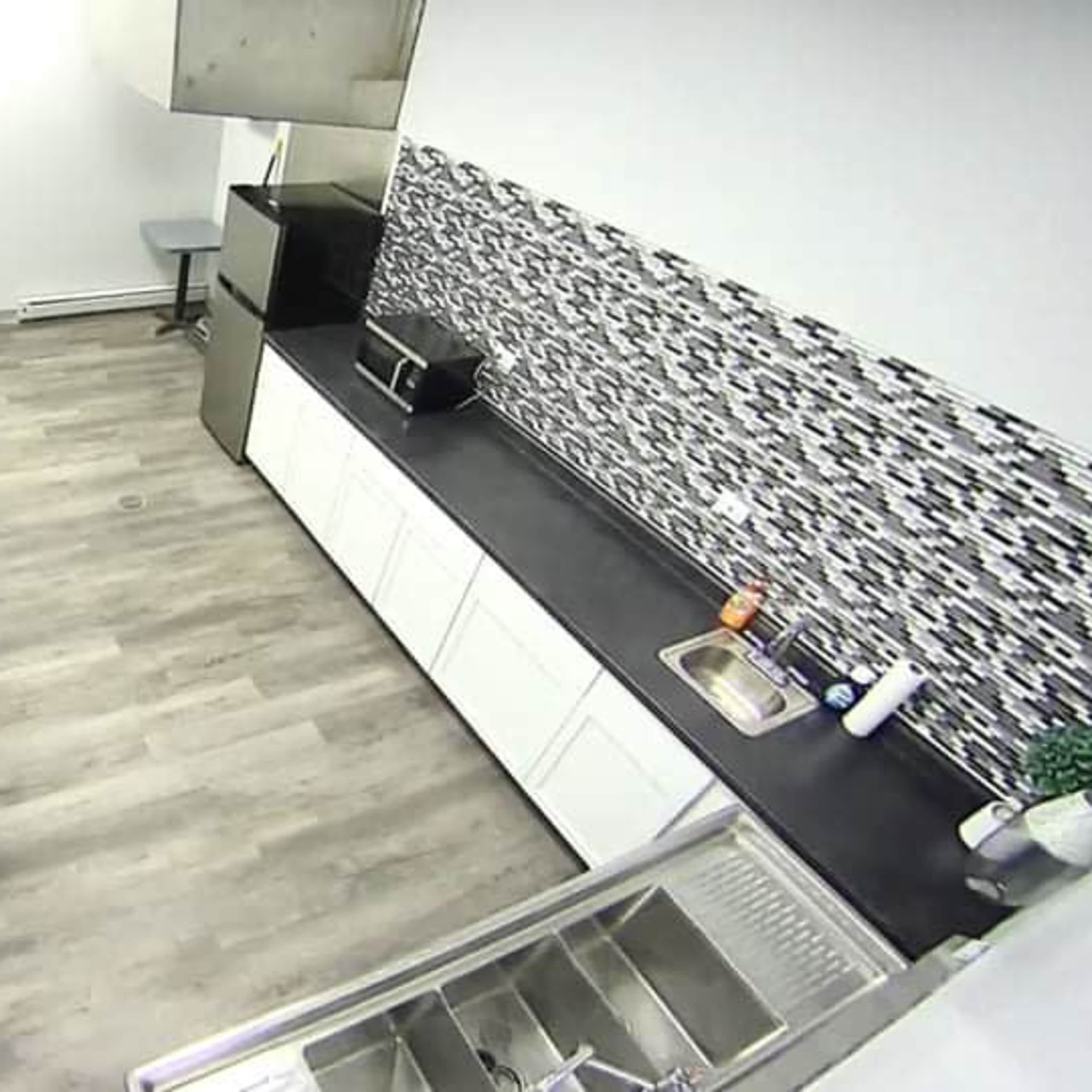 A modern kitchen with a black countertop, white cabinets, and a tiled backsplash, featuring a sink and a microwave.