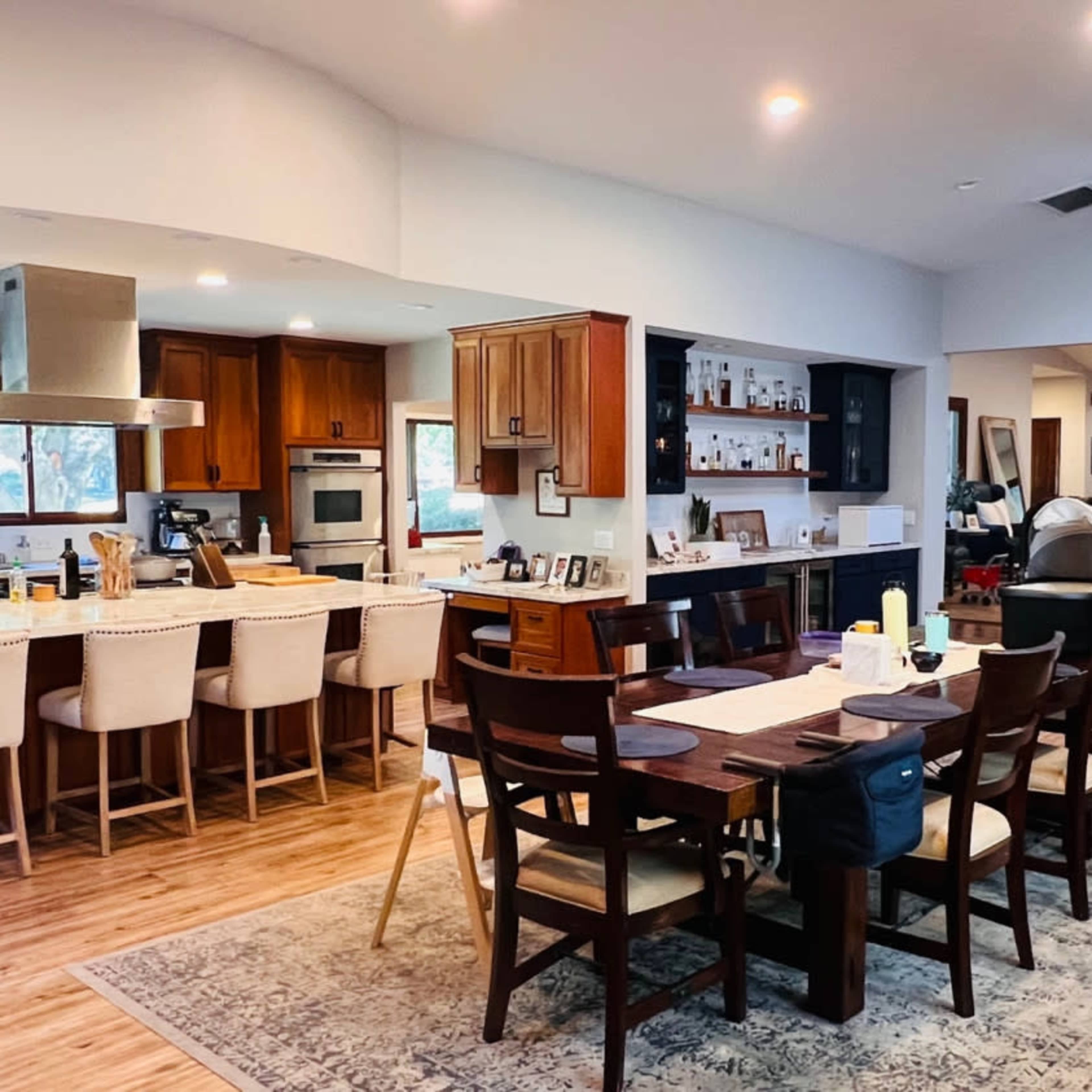 A spacious kitchen and dining area featuring wooden cabinets, a large stone fireplace, a dining table, and a dog on a rug.