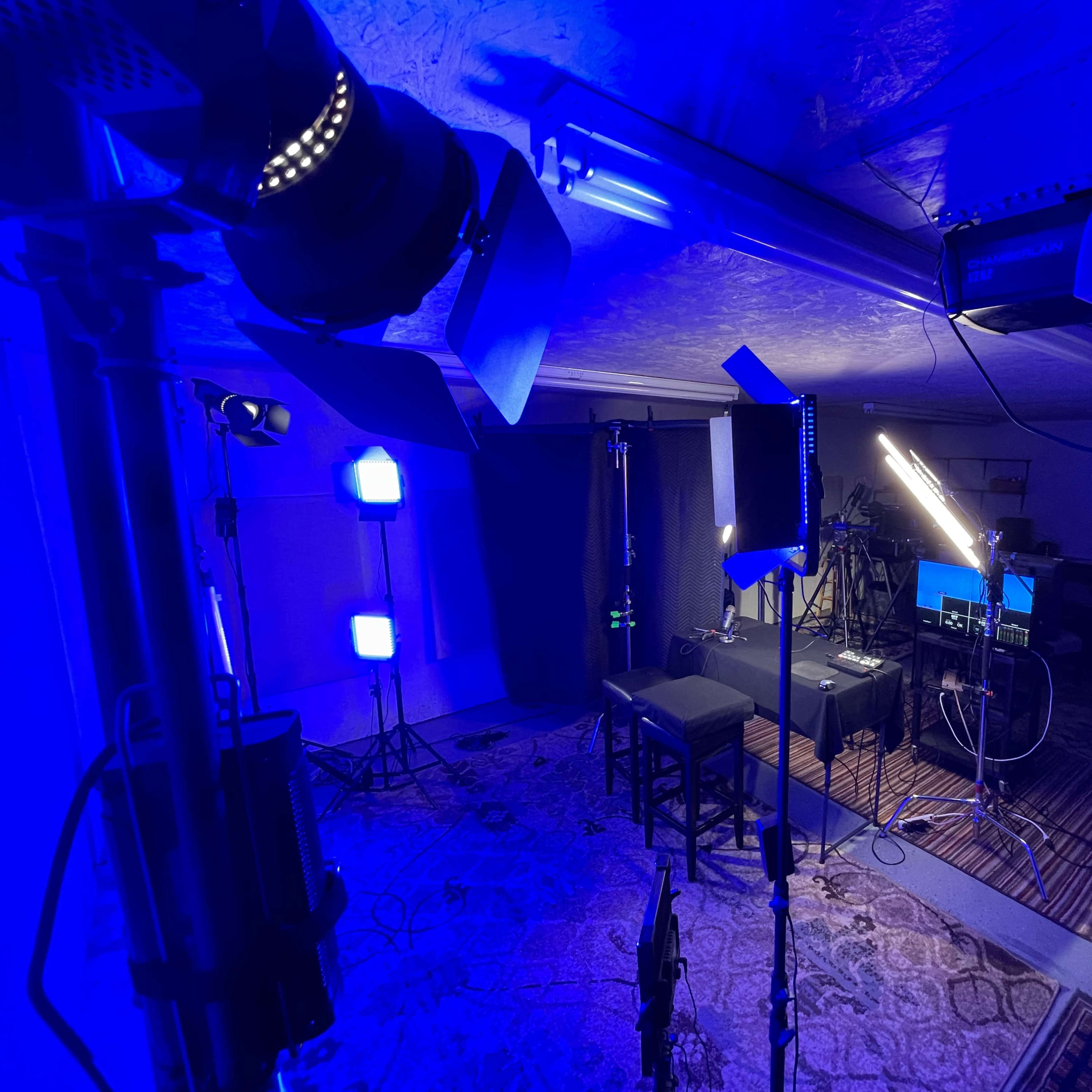 A studio setup with various lighting equipment and a desk area, arranged for a video or photography shoot.