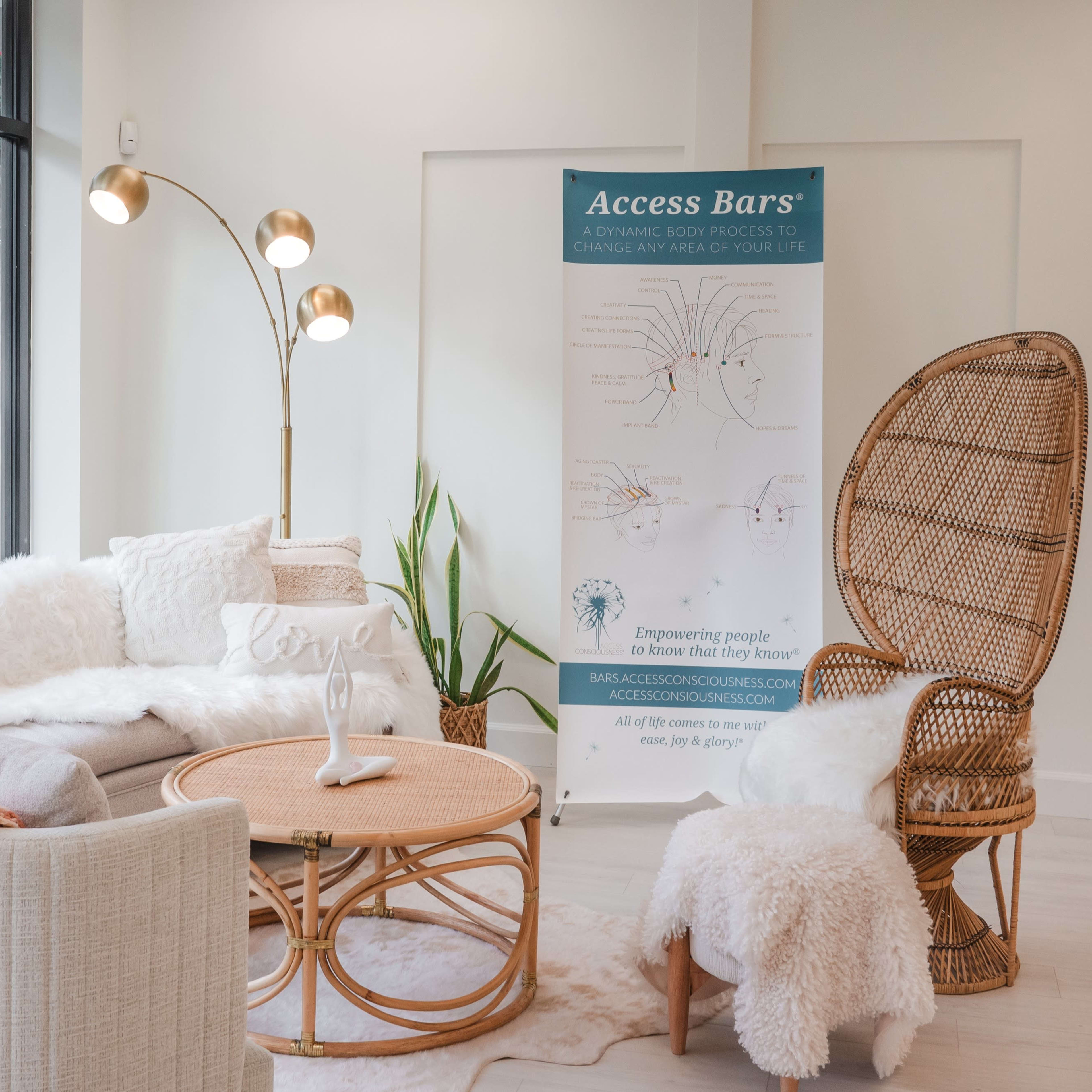 A modern, well-lit lounge area featuring a curved sofa, a rattan chair, a round coffee table, and a banner for "Access Bars" against a large window.