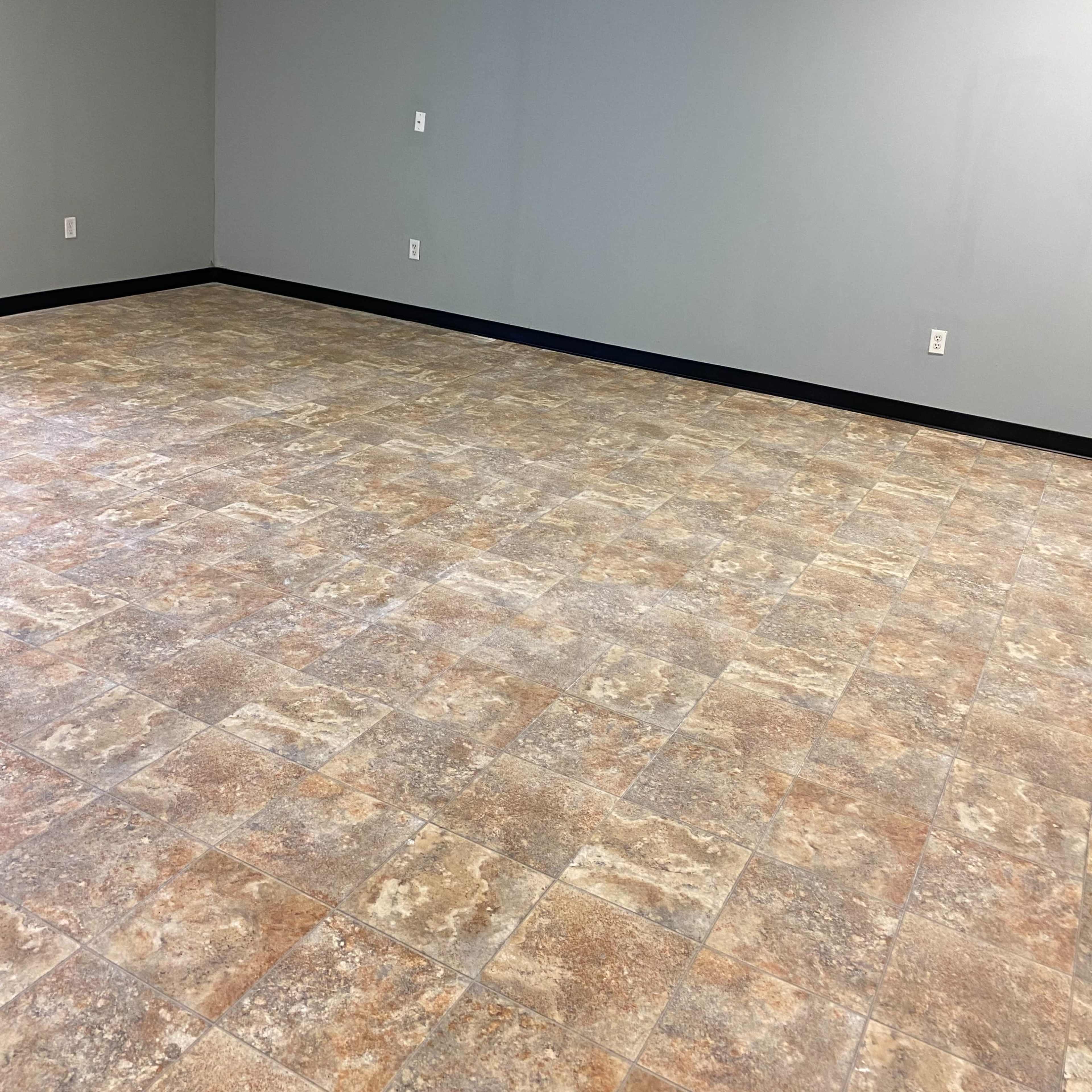 A spacious, empty room with light gray walls and a patterned tile floor.