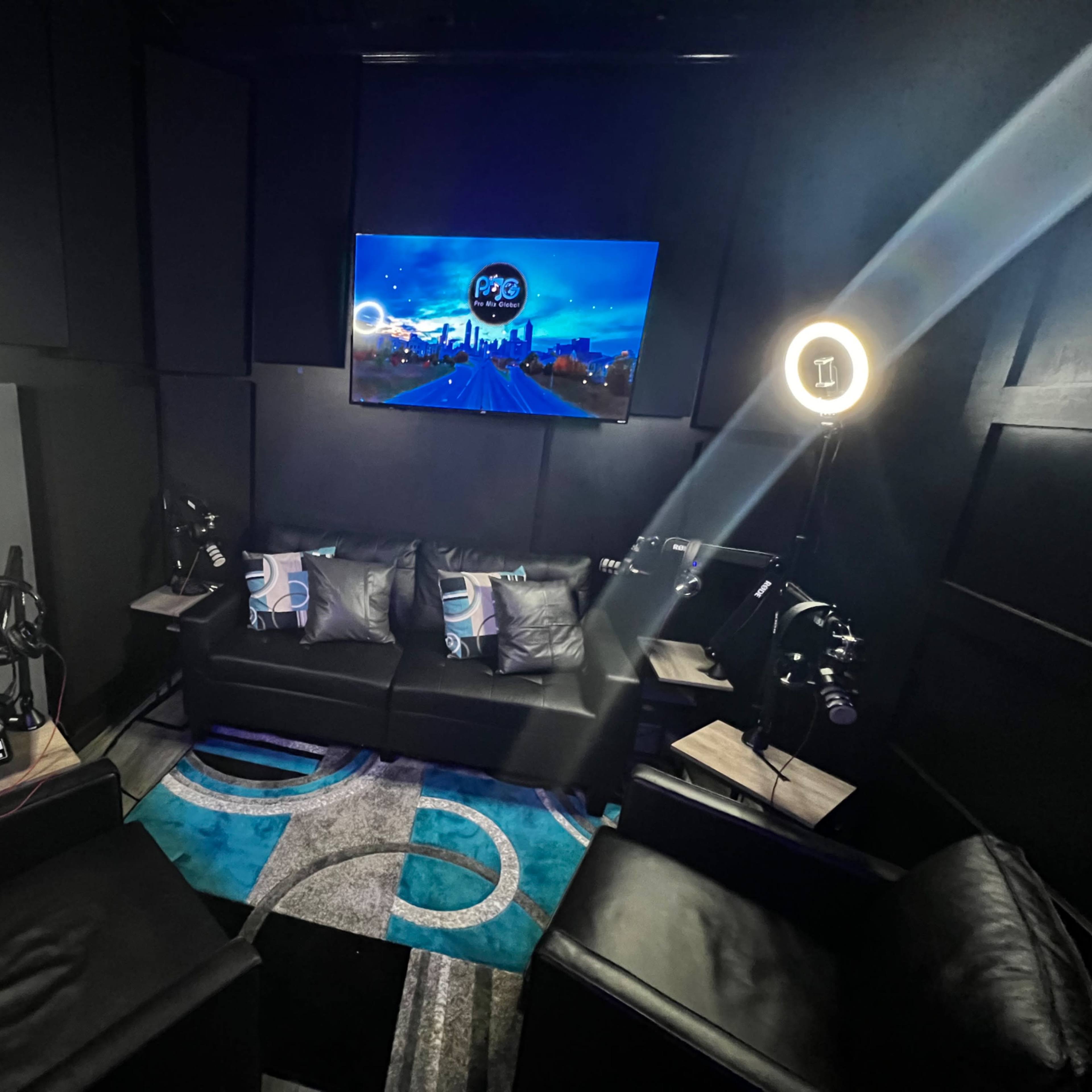 A recording studio with a sofa, two chairs, and technical equipment, all surrounded by soundproofing panels.