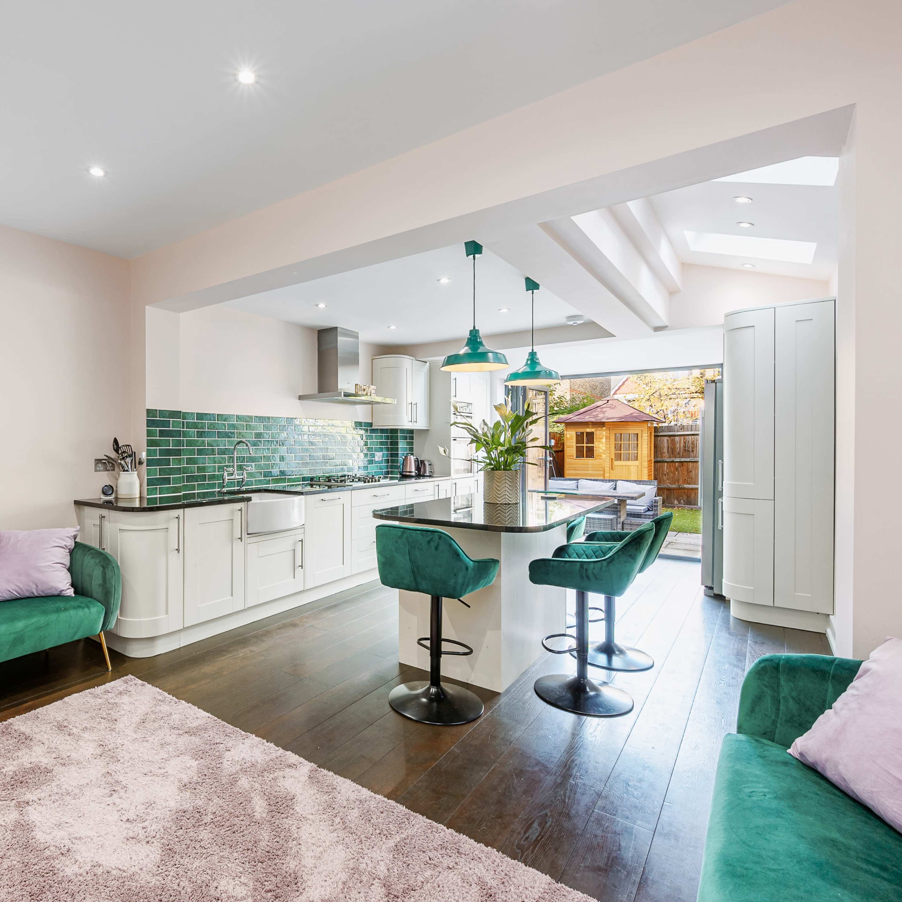 A modern kitchen features green accents, a bar with stools, and a spacious layout with large windows.