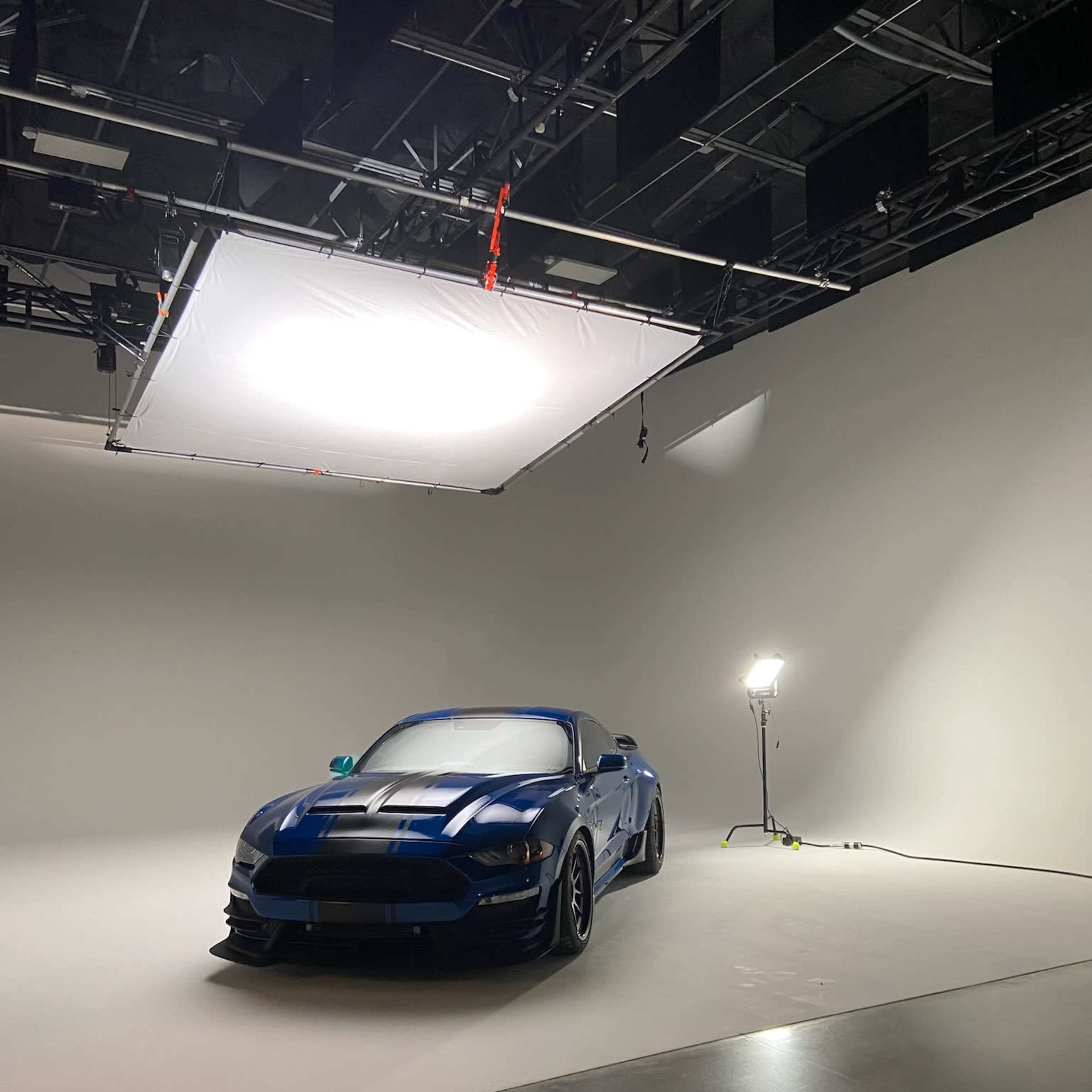 A blue sports car is positioned in a well-lit studio with a plain white backdrop.