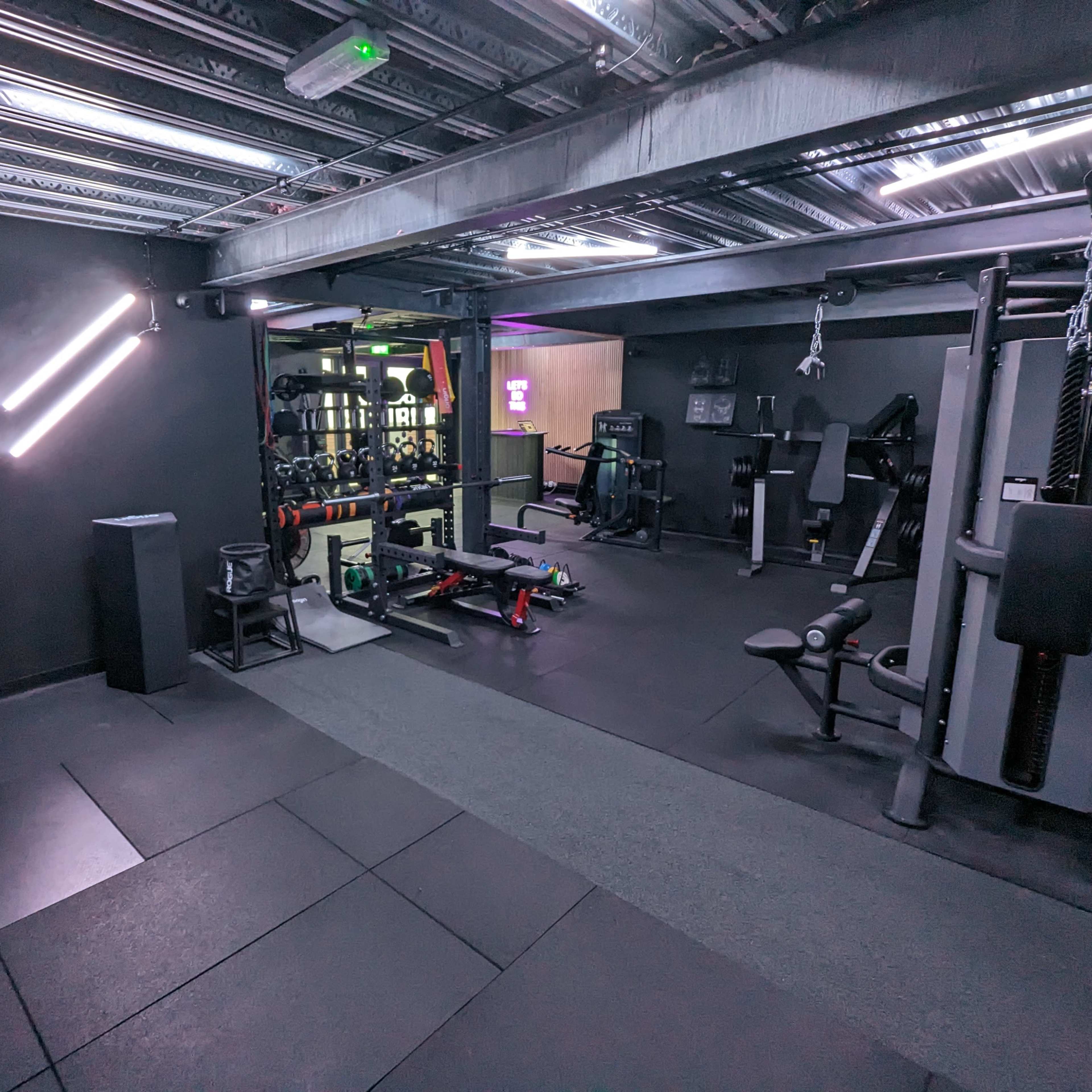 A modern gym interior with various fitness equipment arranged on a dark floor under artificial lighting.