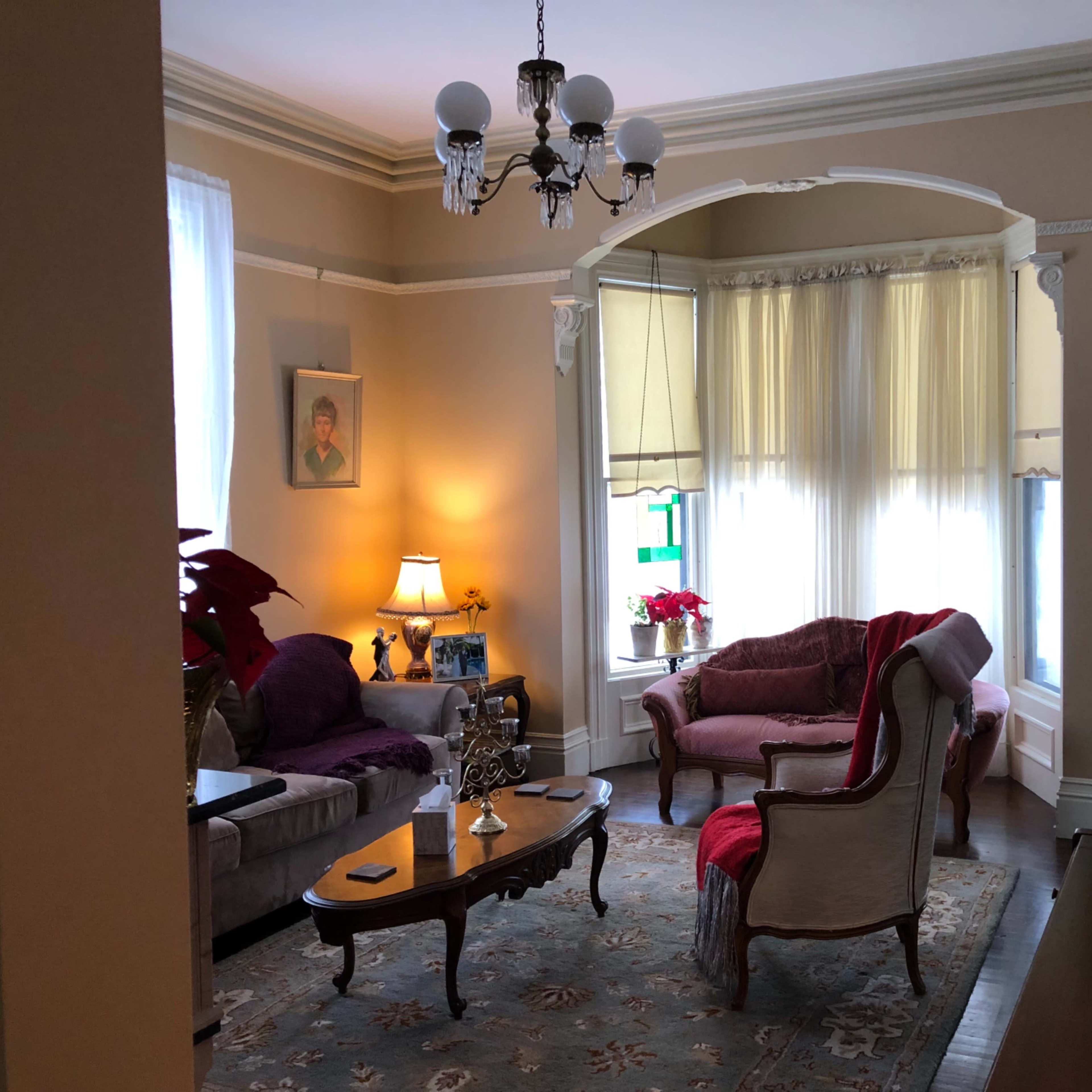 A cozy living room with a chandelier, a sofa, and a chair arranged around a coffee table, complemented by large windows and various decorations.
