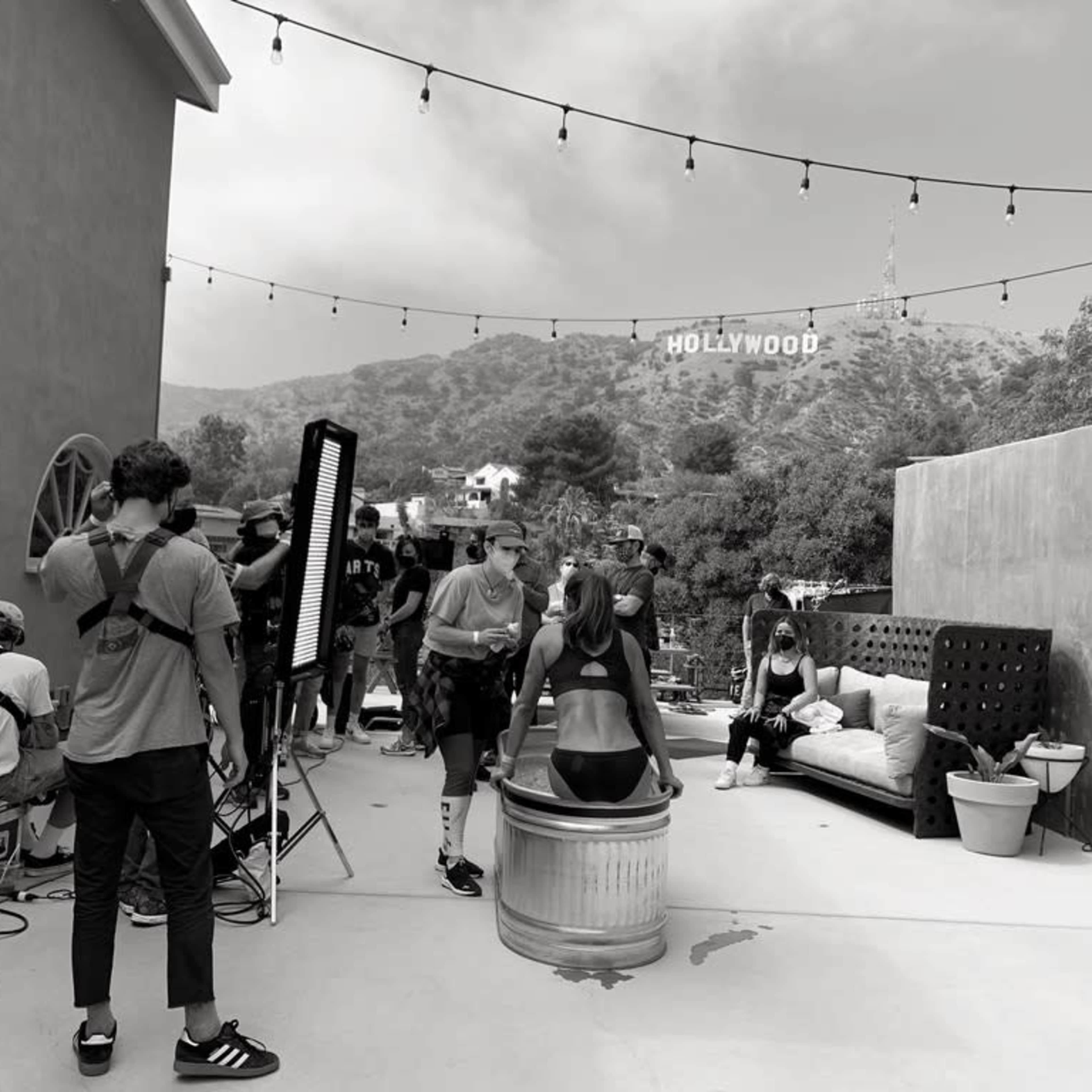 A film crew operates on a set with the Hollywood sign visible in the background.
