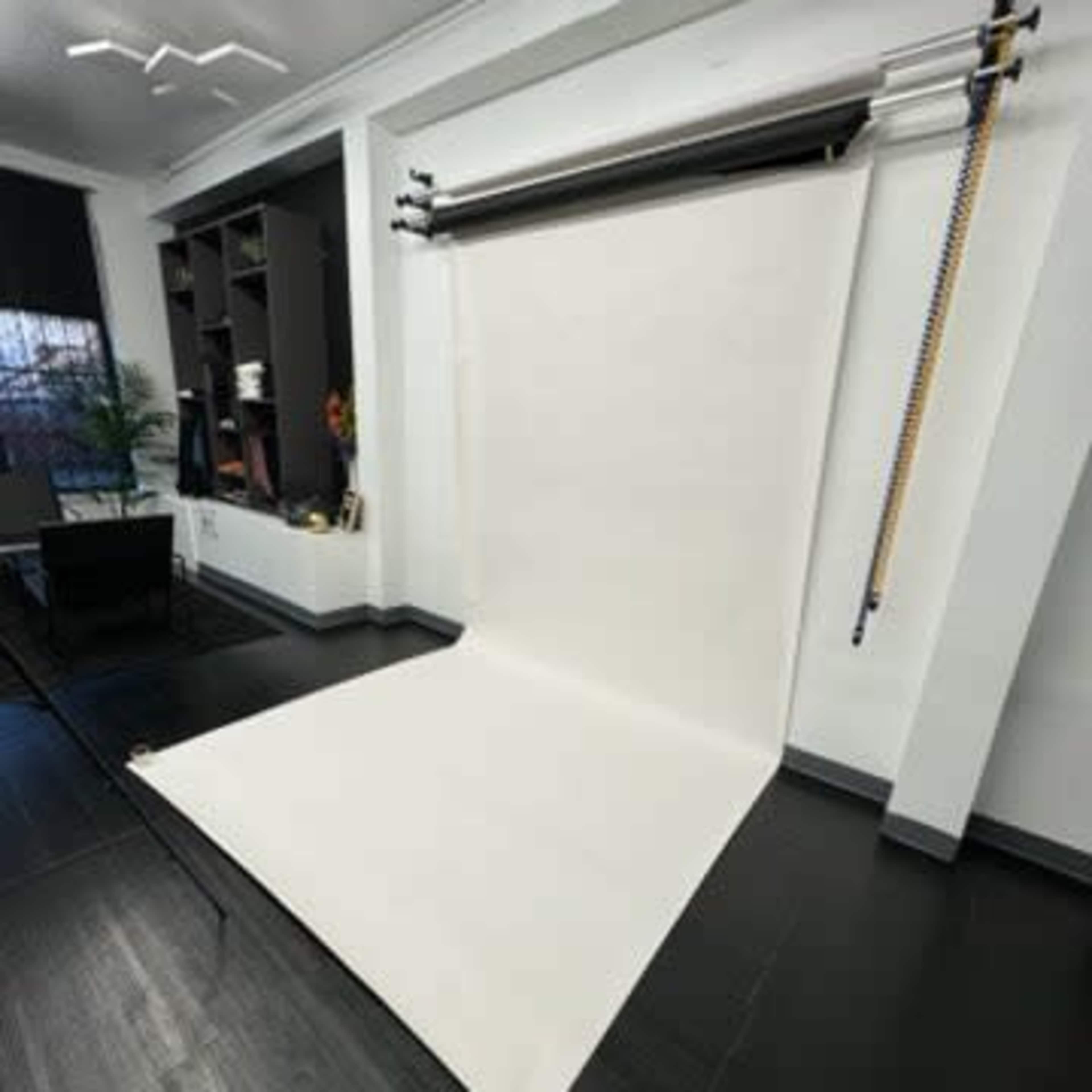 A photography studio setup with a white backdrop extending to the floor and a shelf with various items in the background.