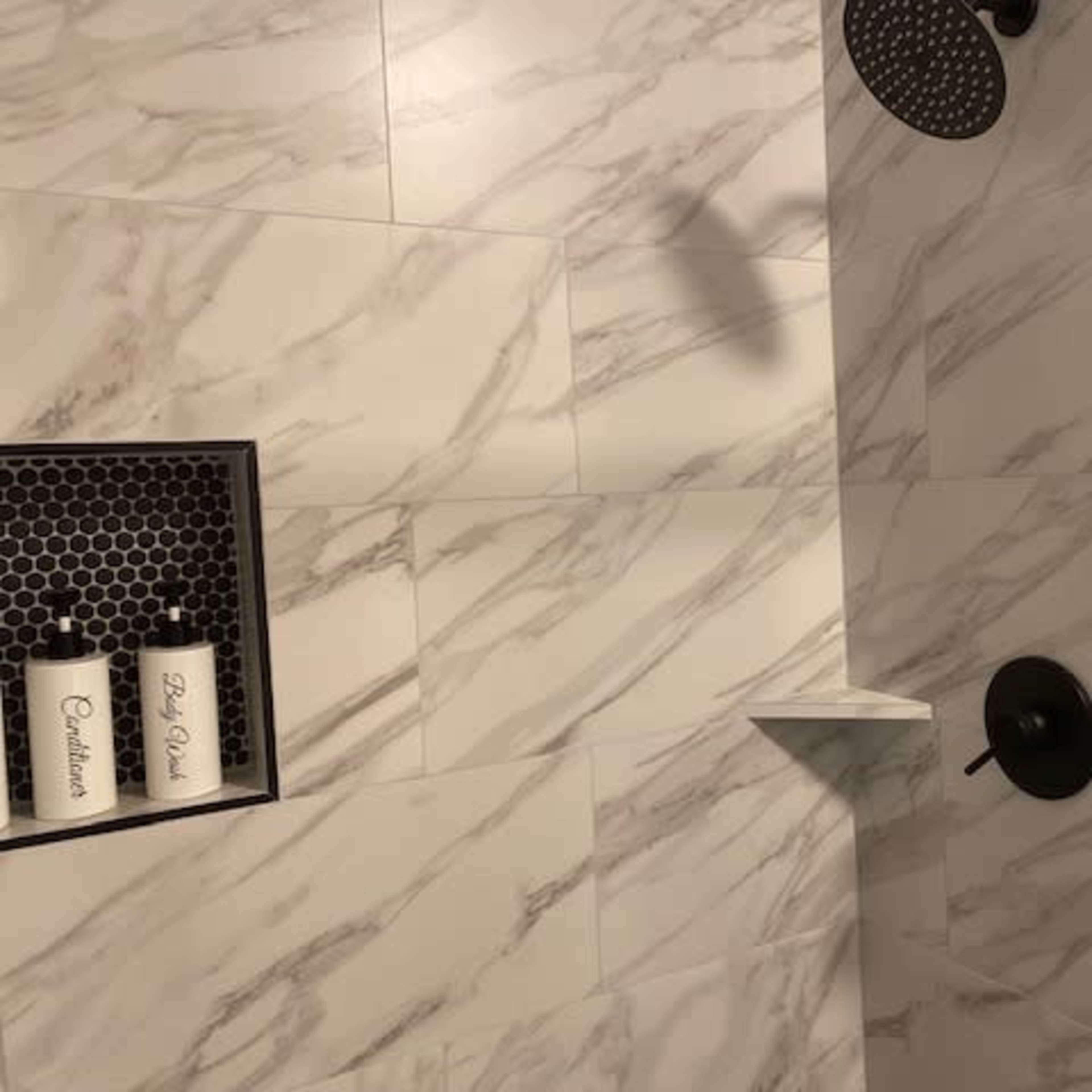 A modern shower area with marble-patterned tiles, a black showerhead, and a shelf holding white containers.
