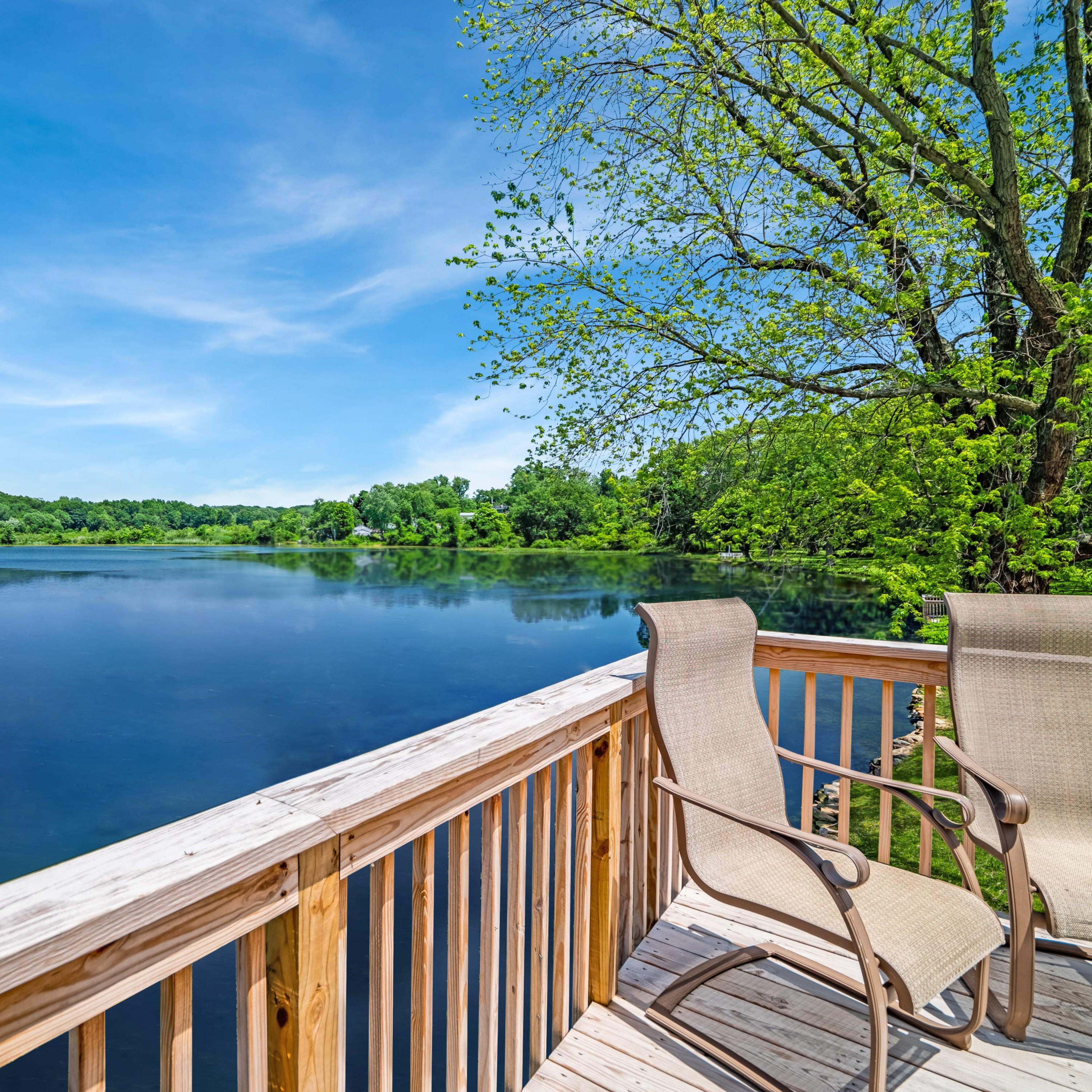 A wooden deck with two chairs overlooks a calm lake surrounded by trees.
