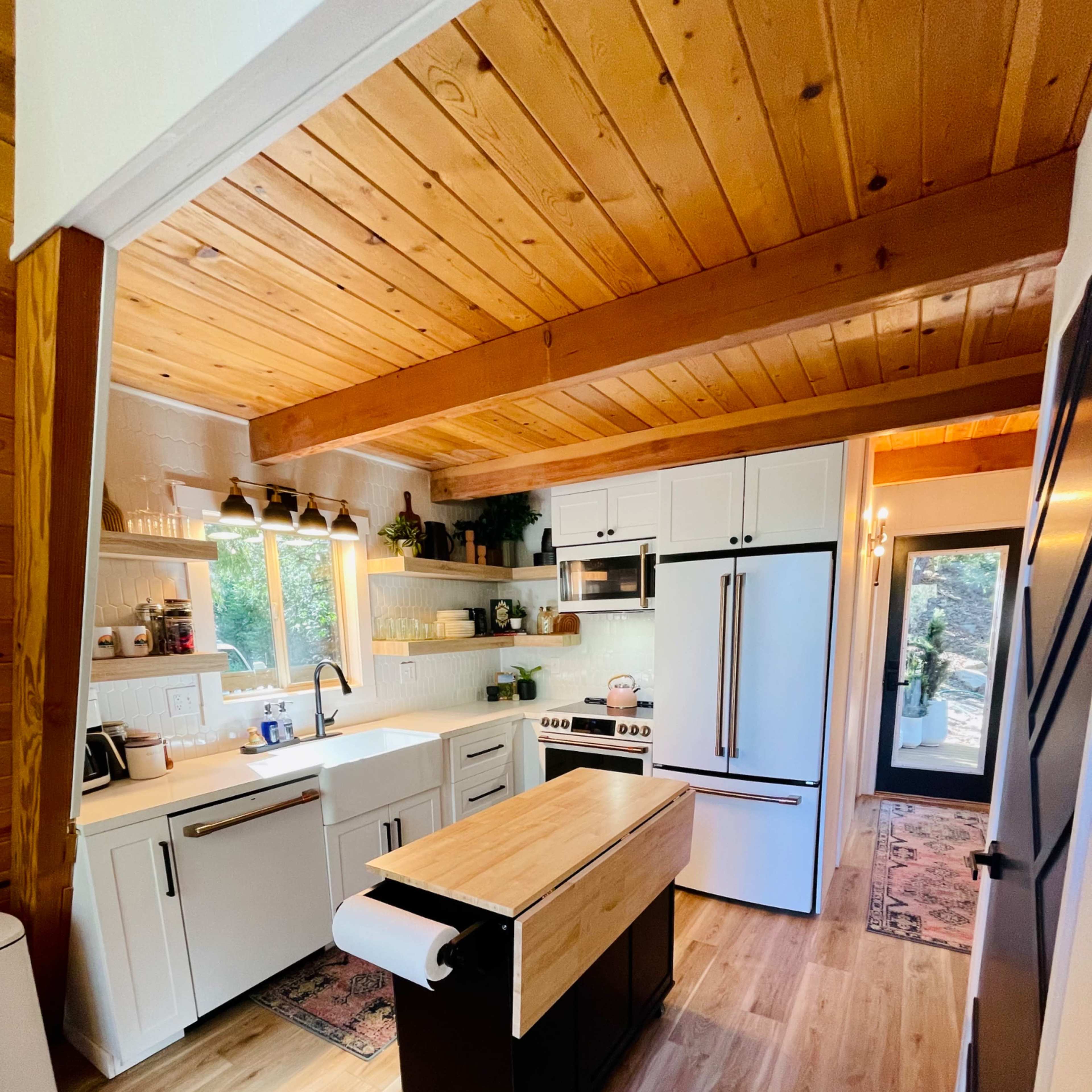 A modern kitchen with white cabinetry, a central wooden island, and large windows overlooking a natural view.