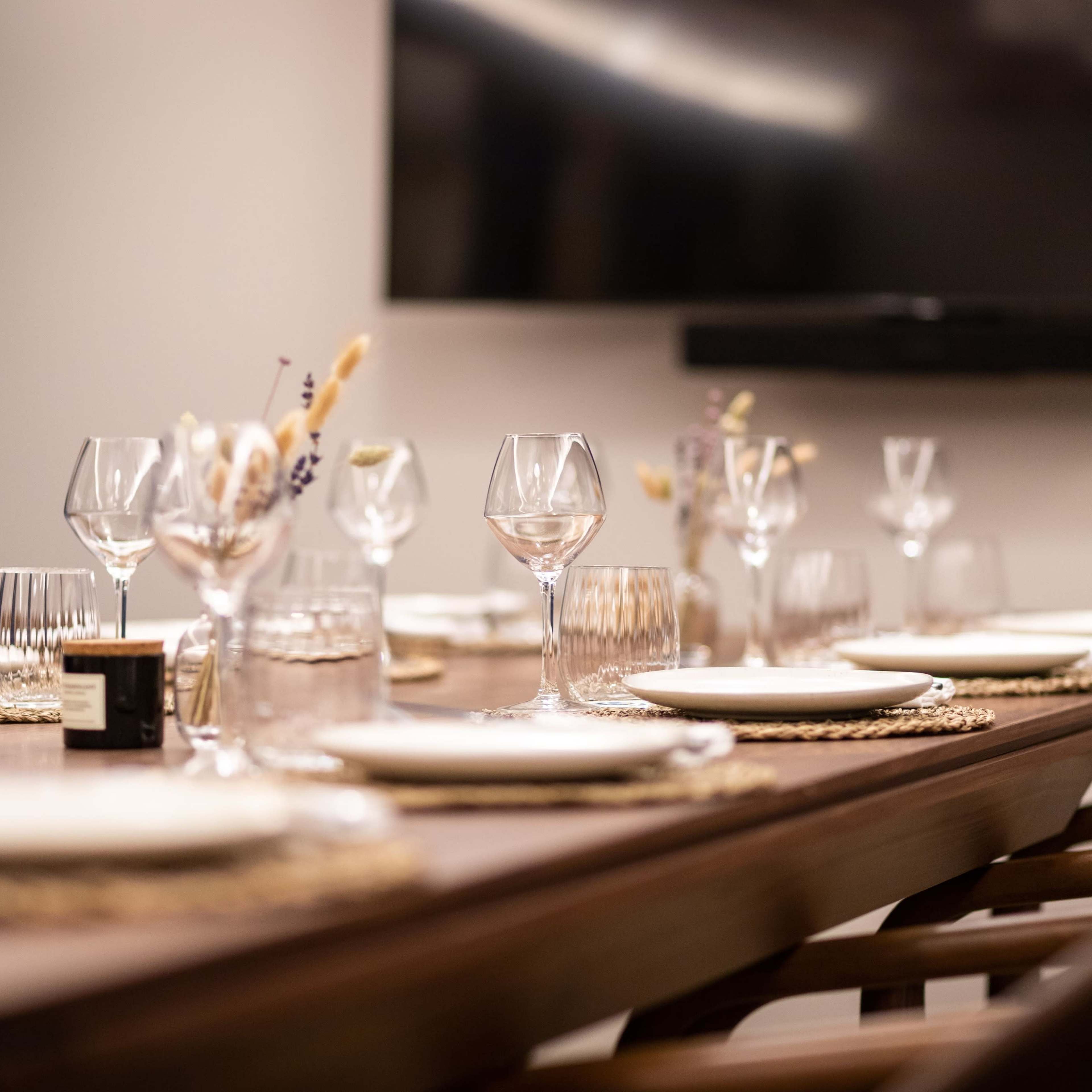 A long dining table is set with plates, glassware, and decorative elements in a well-lit room.